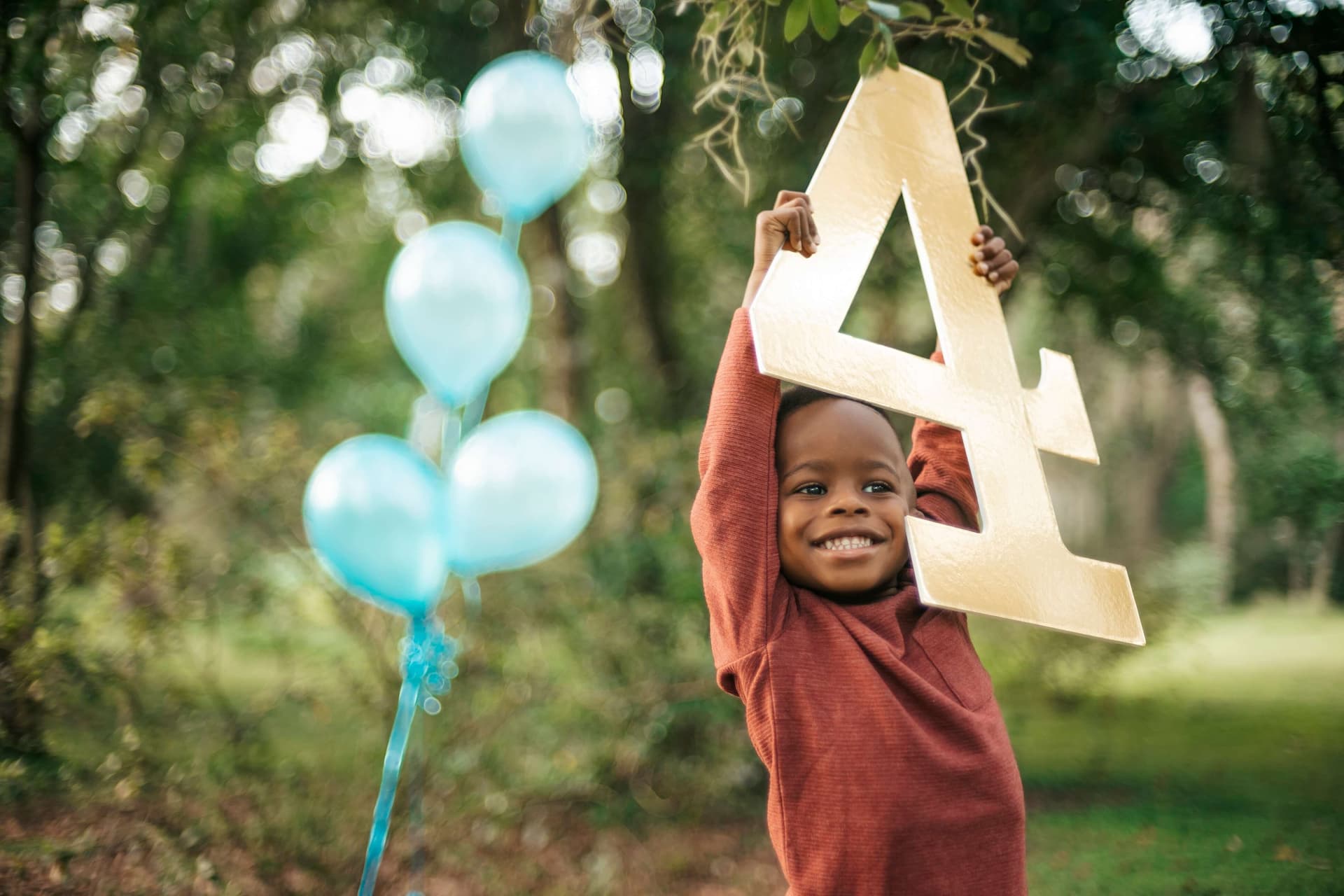 child holding up a cardboard number 4 with balloons next to him