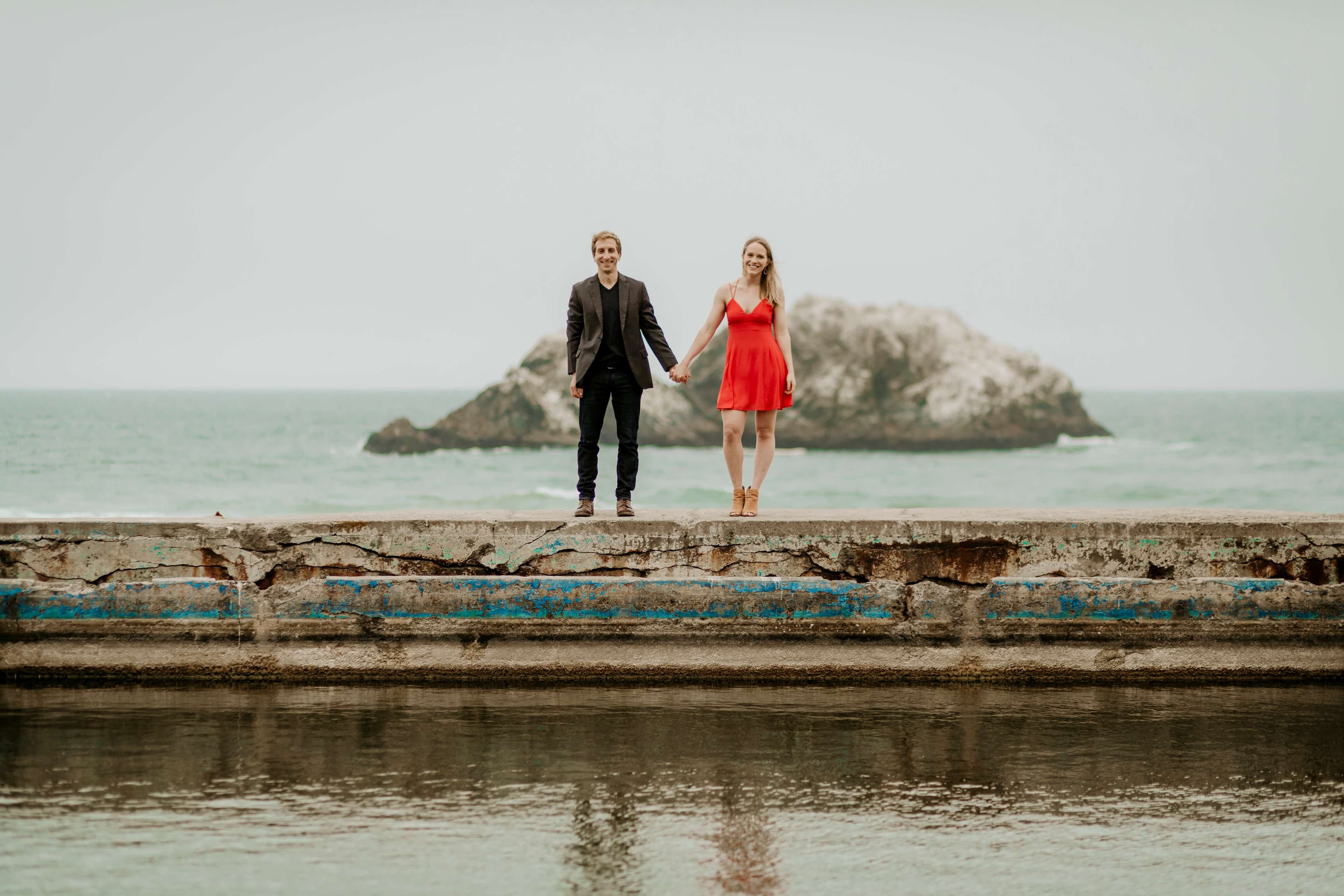 two people posing for an engagement photoshoot on a beach wall