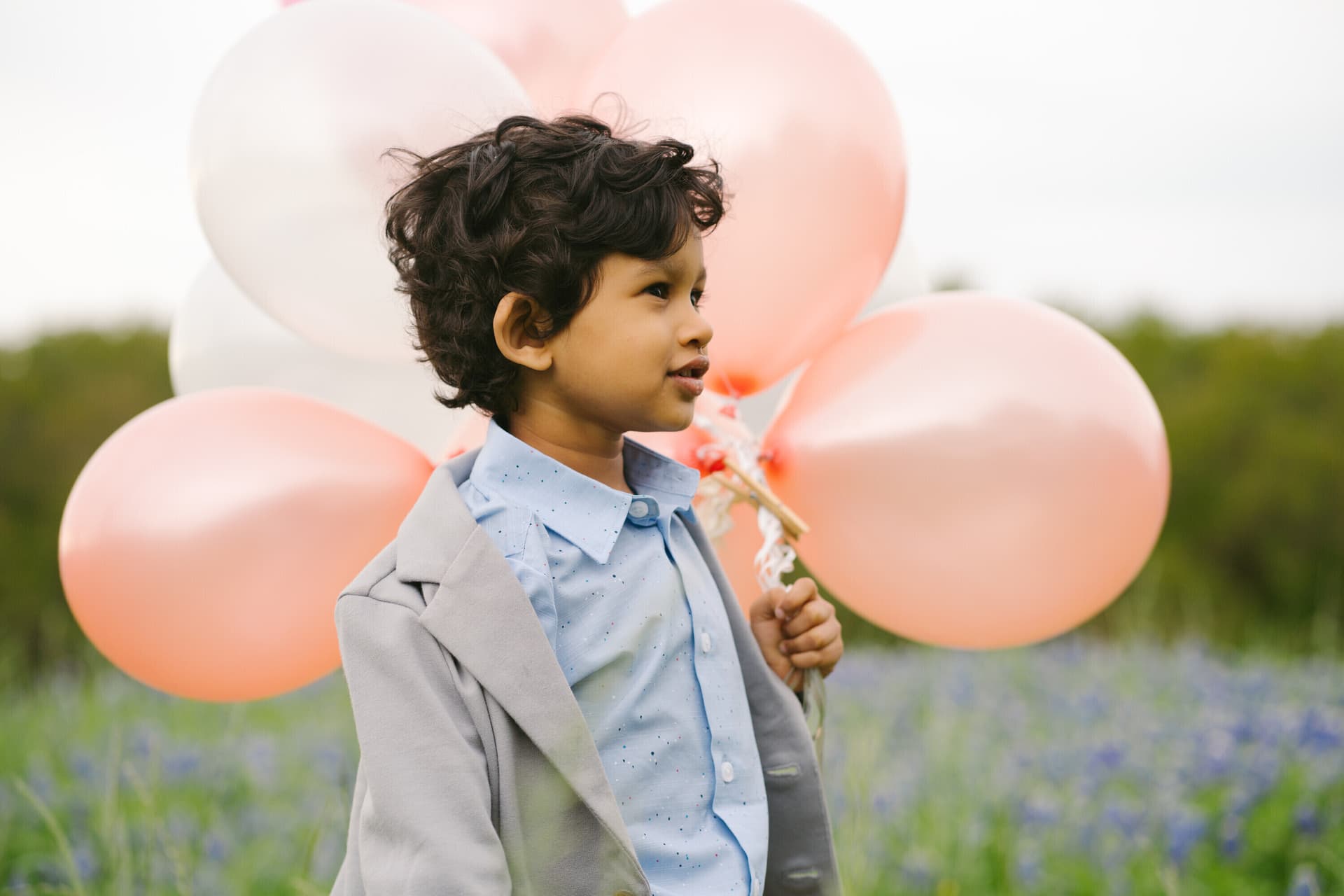 Young child holding pink and white balloons in a bluebonnet field
