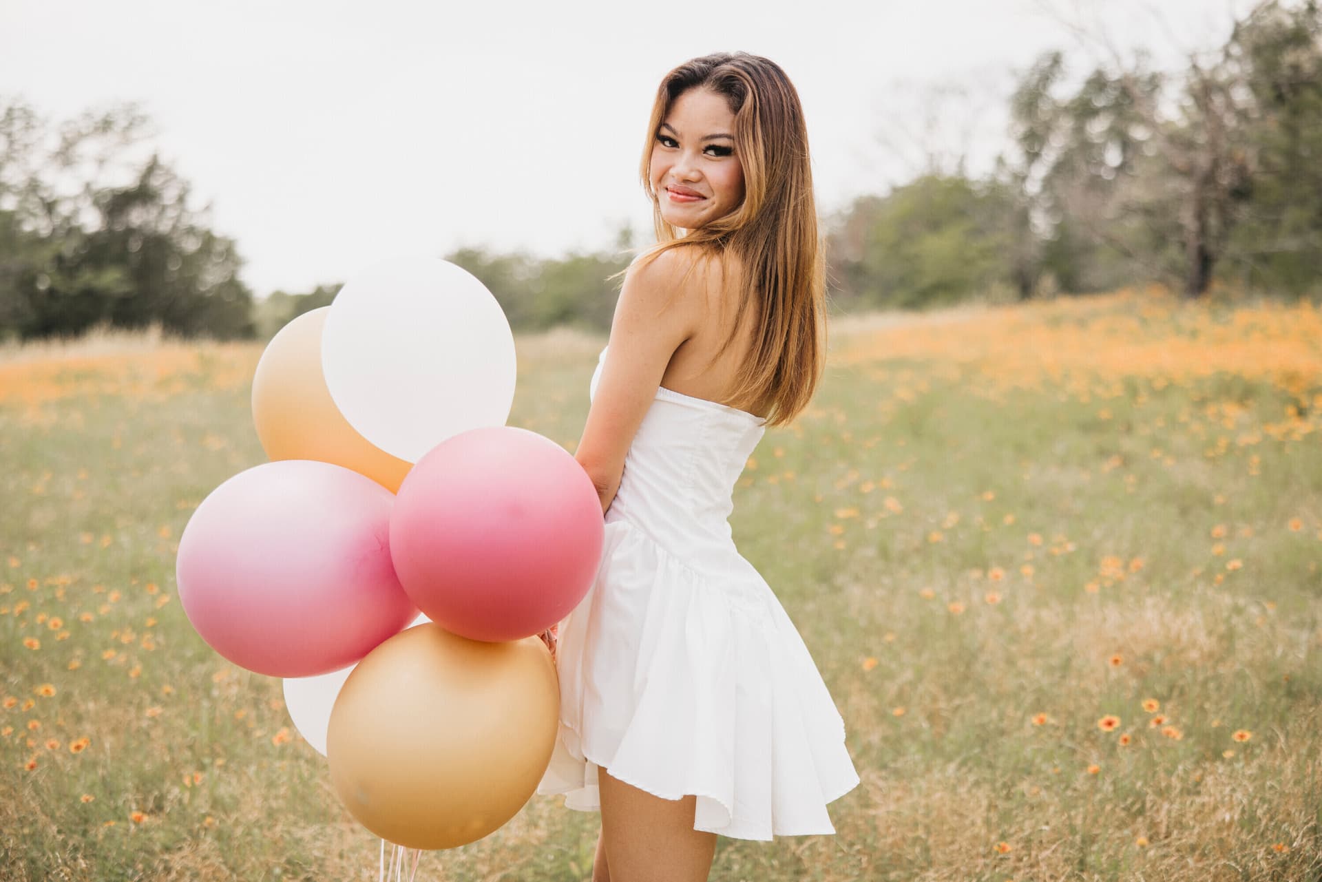 Young woman in a white dress holding colorful balloons in a wildflower field