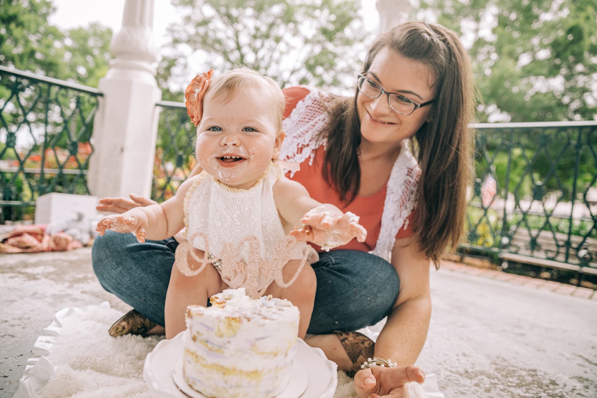 Mother watching her baby enjoy a cake smash birthday session outdoors