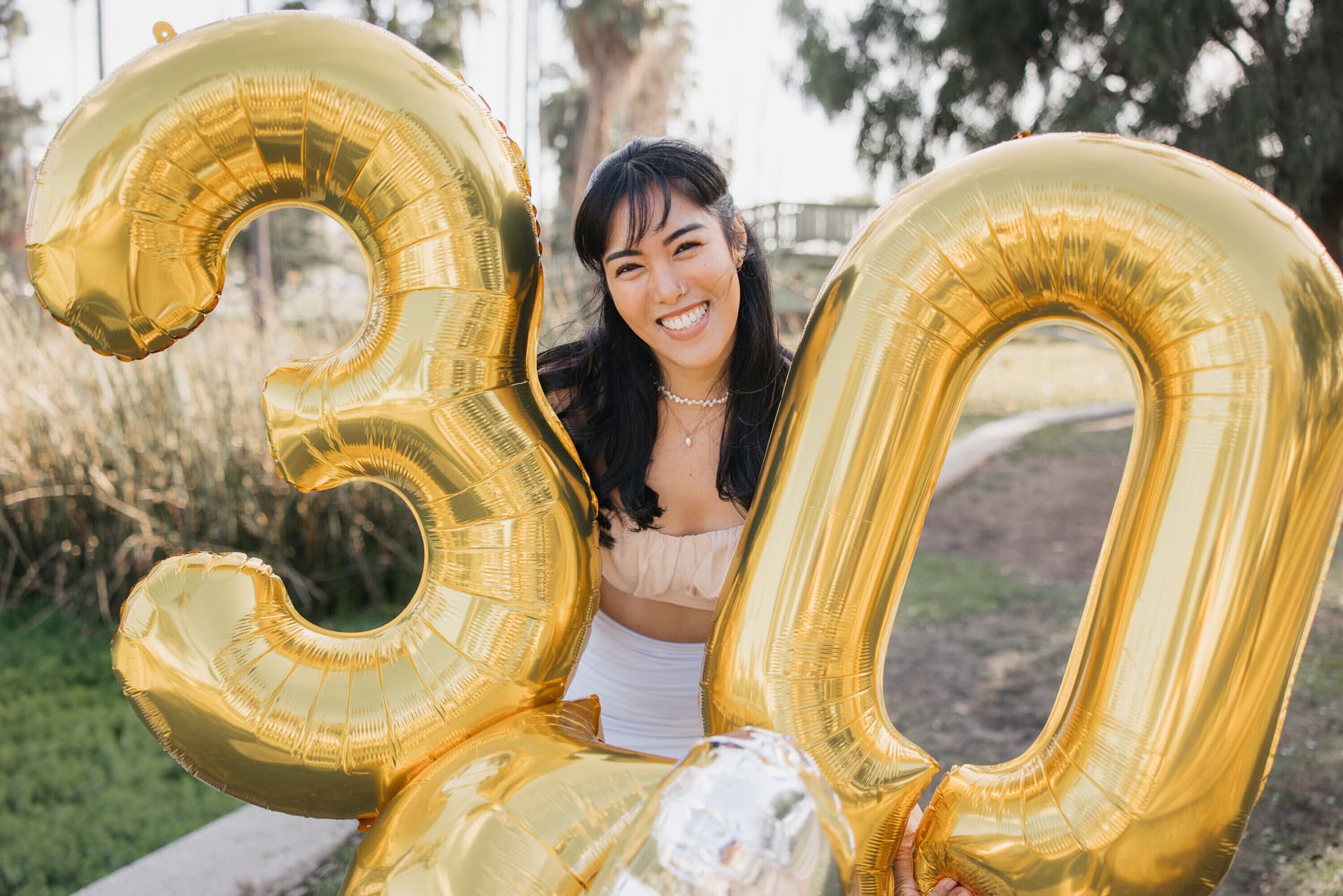 Woman holding large gold '30' number balloons for a milestone birthday portrait