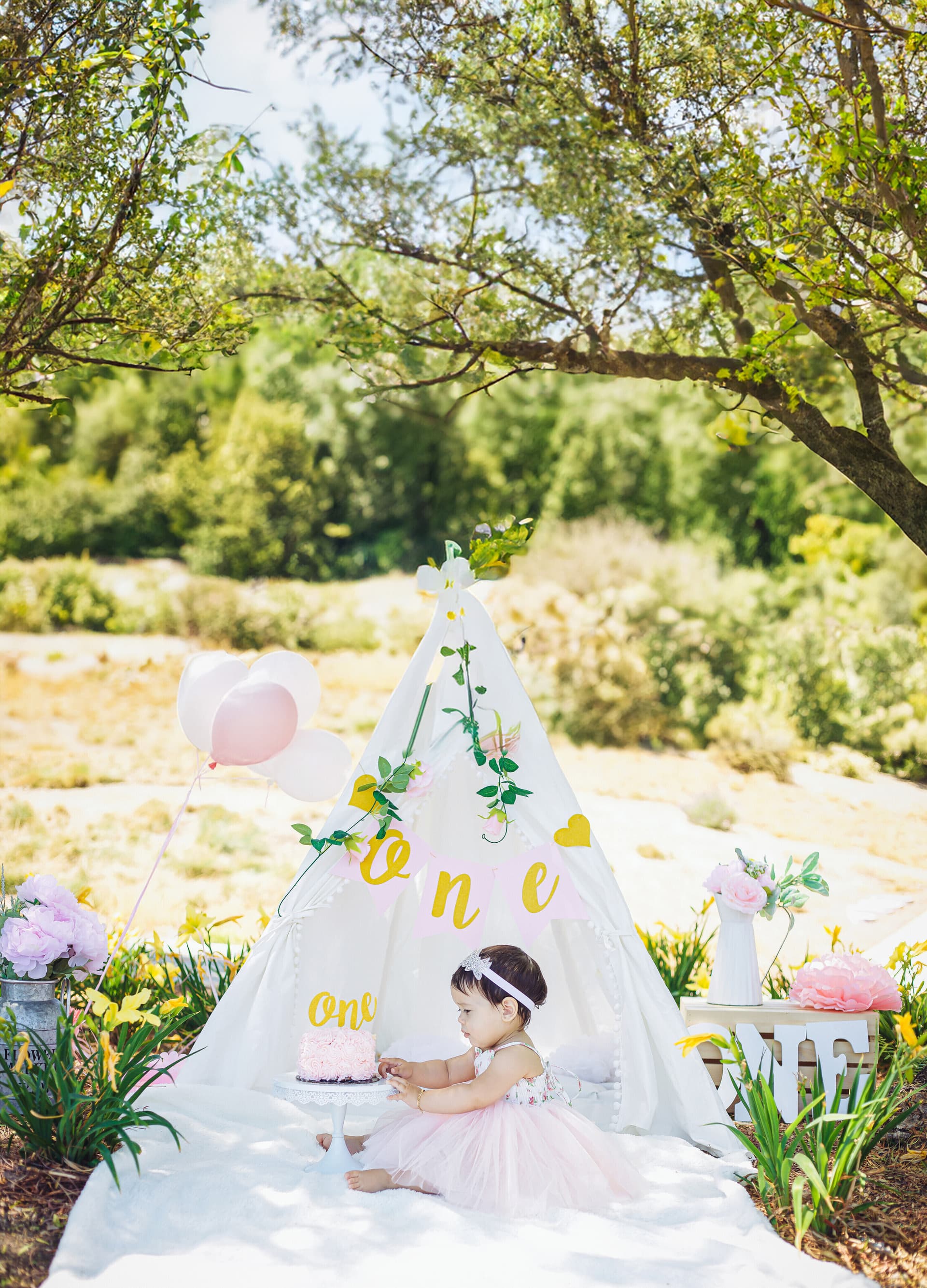 Baby girl's first birthday outdoor setup with a white teepee and floral decorations