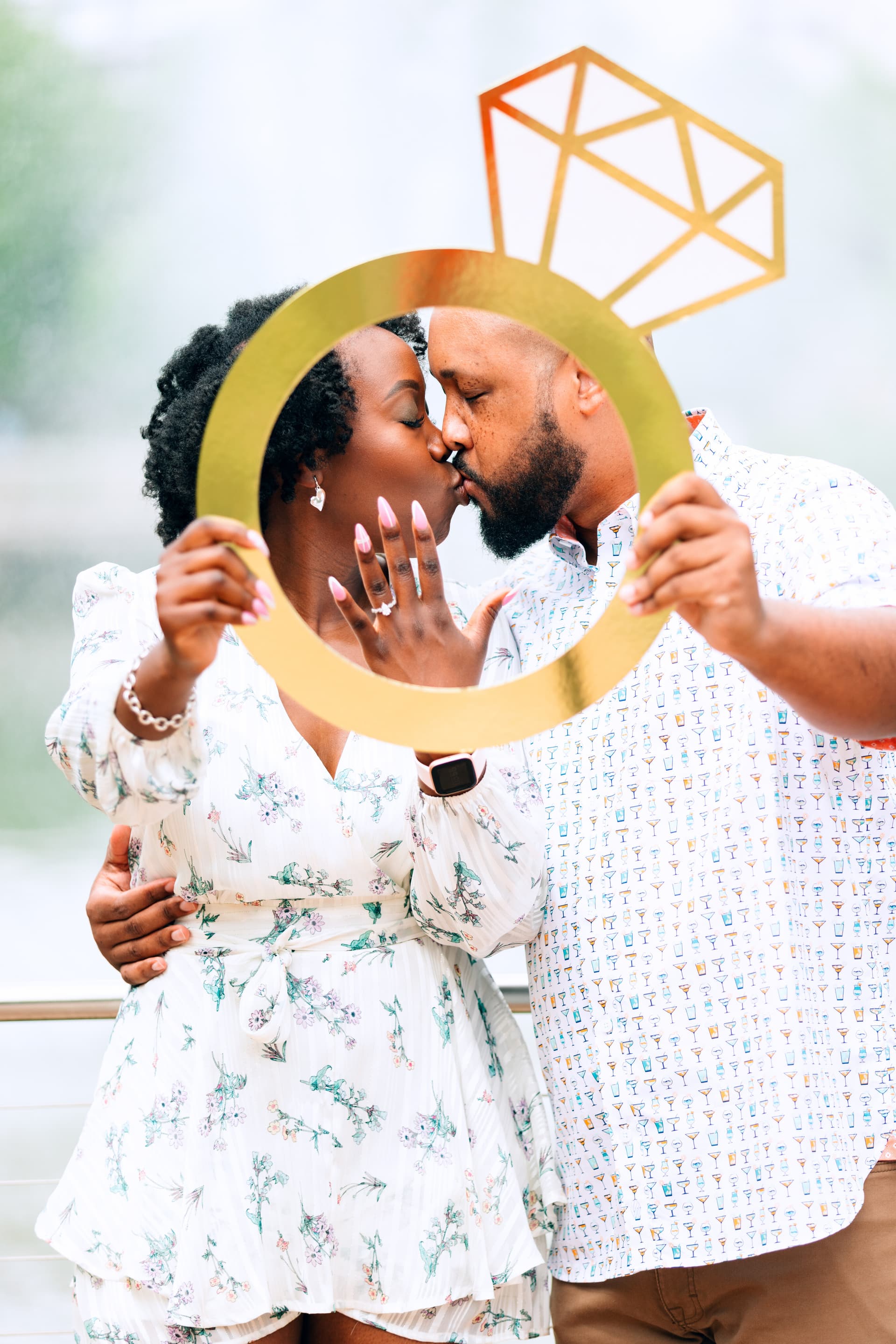Engaged couple kissing while holding a gold ring-shaped photo prop