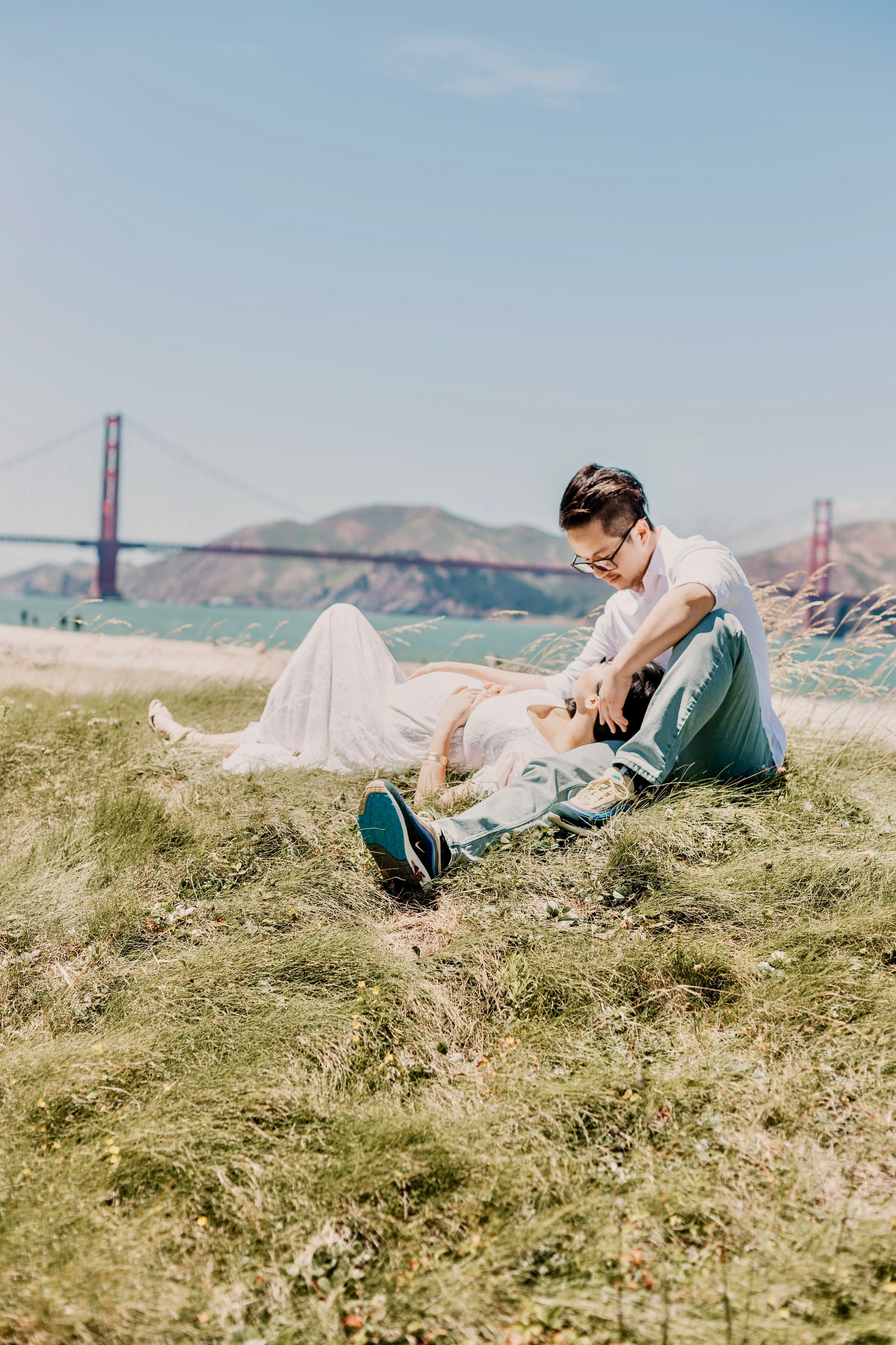 A couple relaxing on a grassy hillside with the Golden Gate Bridge visible in the background
