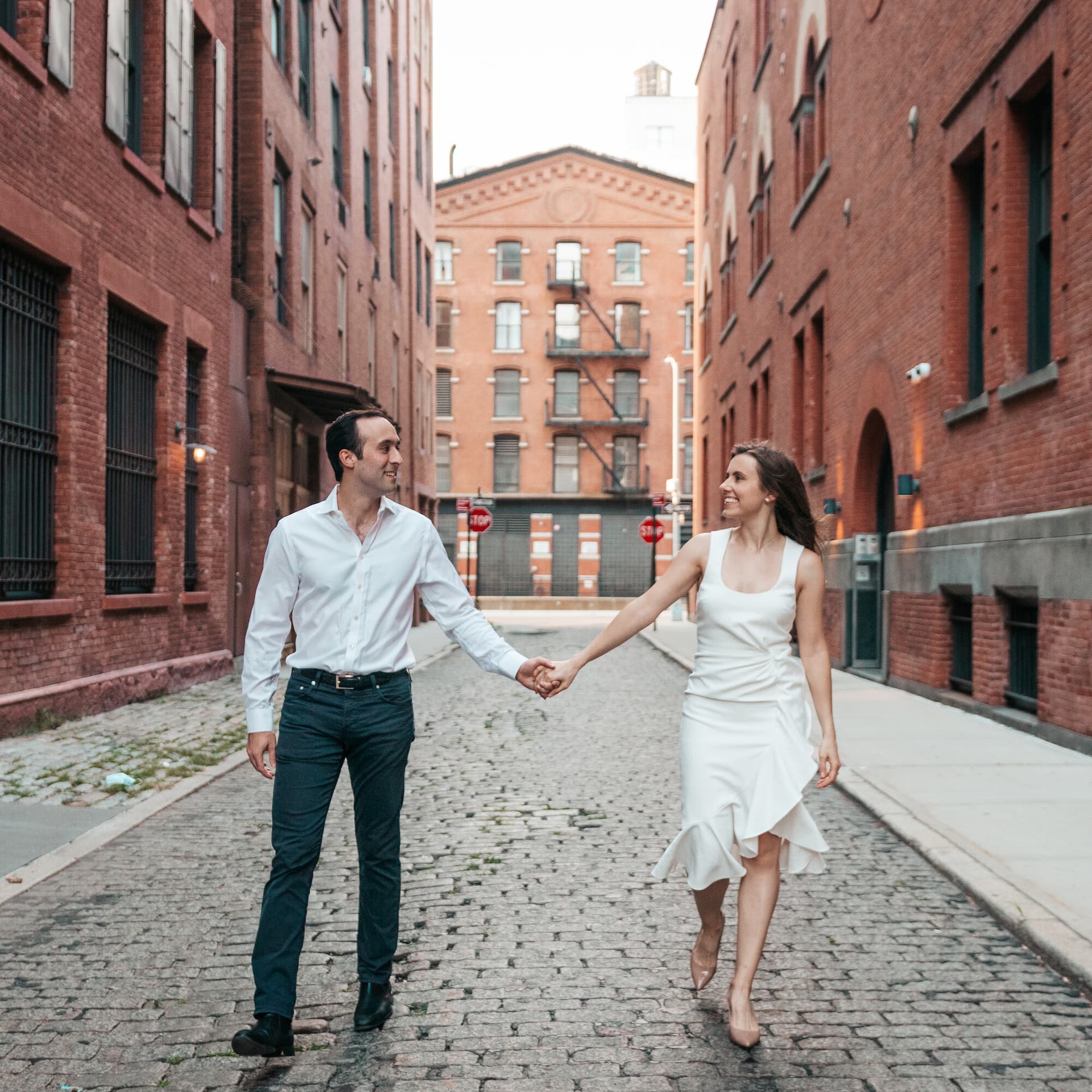 A couple holding hands and walking together down a cobblestone alley between brick buildings