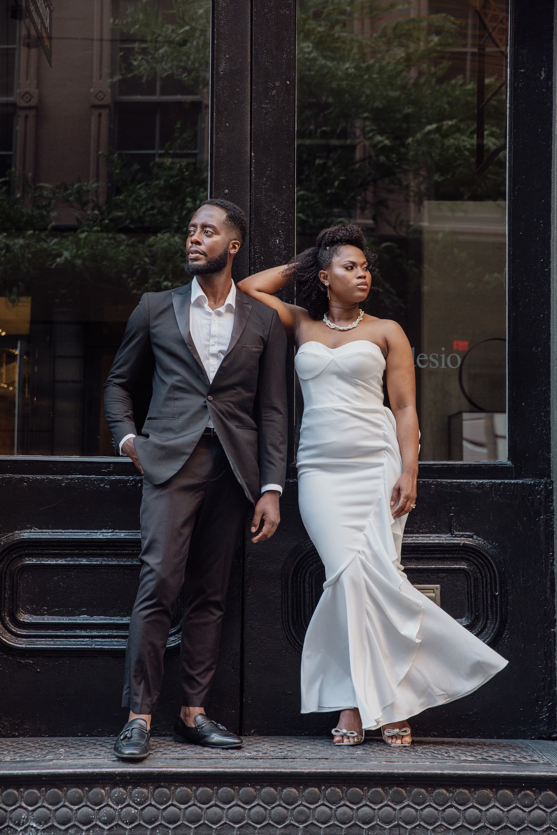 A well-dressed couple posing on a city street, the man in a suit and the woman in a white gown