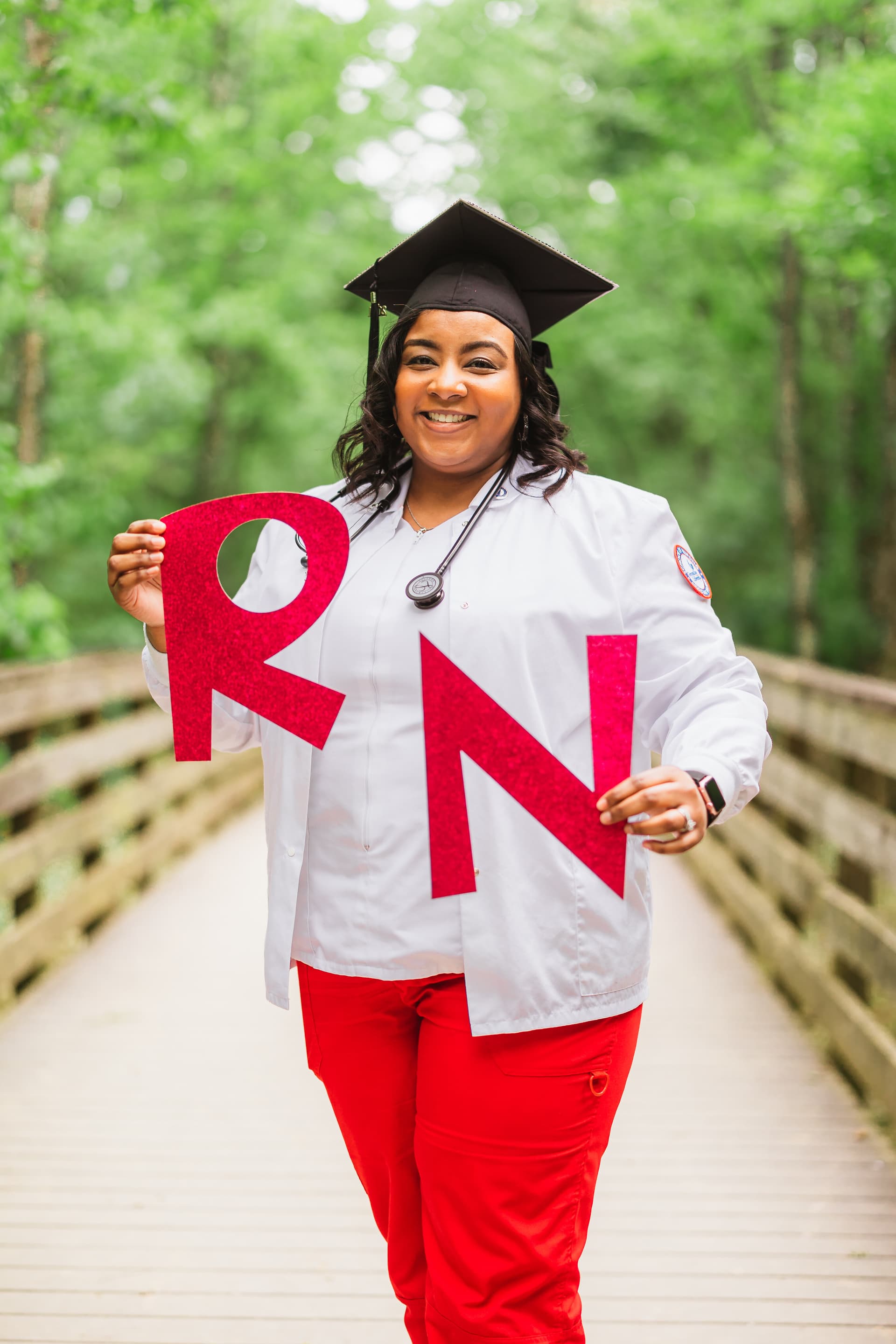 Nursing graduate in scrubs holding RN letter props outdoors
