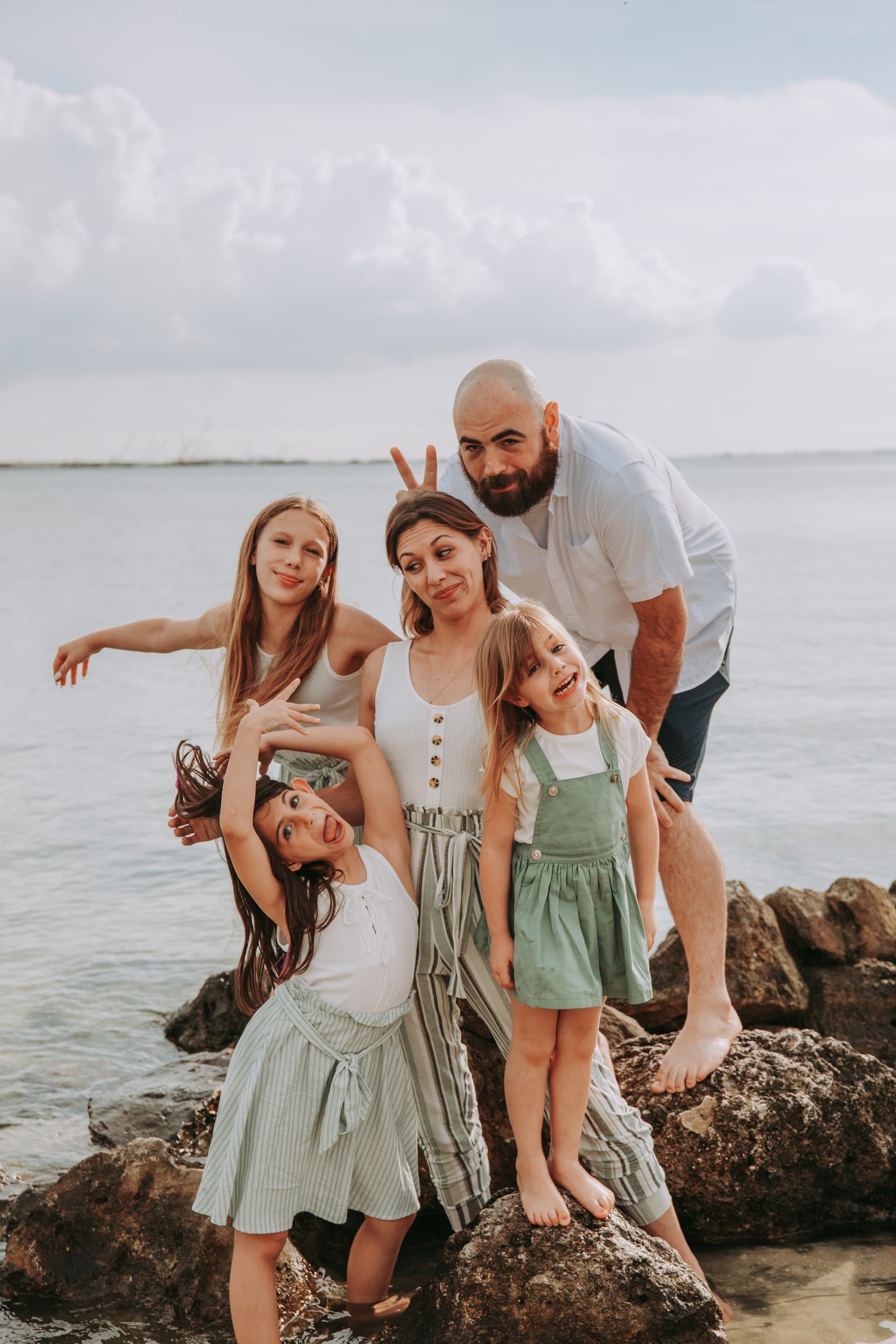 Family of five posing playfully on a rocky beach shoreline