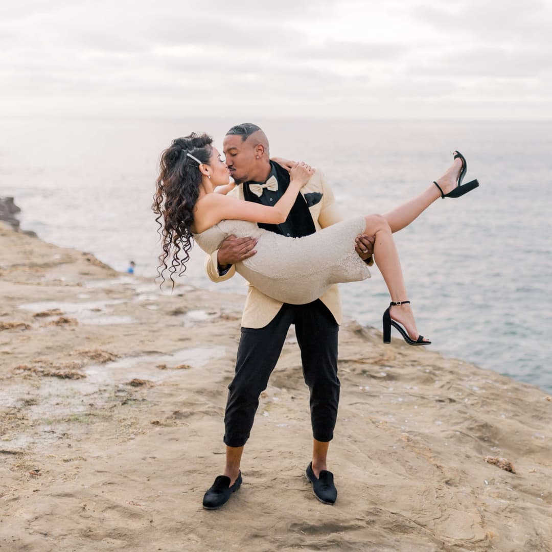 man lifting and kissing woman on a cliff overlooking a lake 