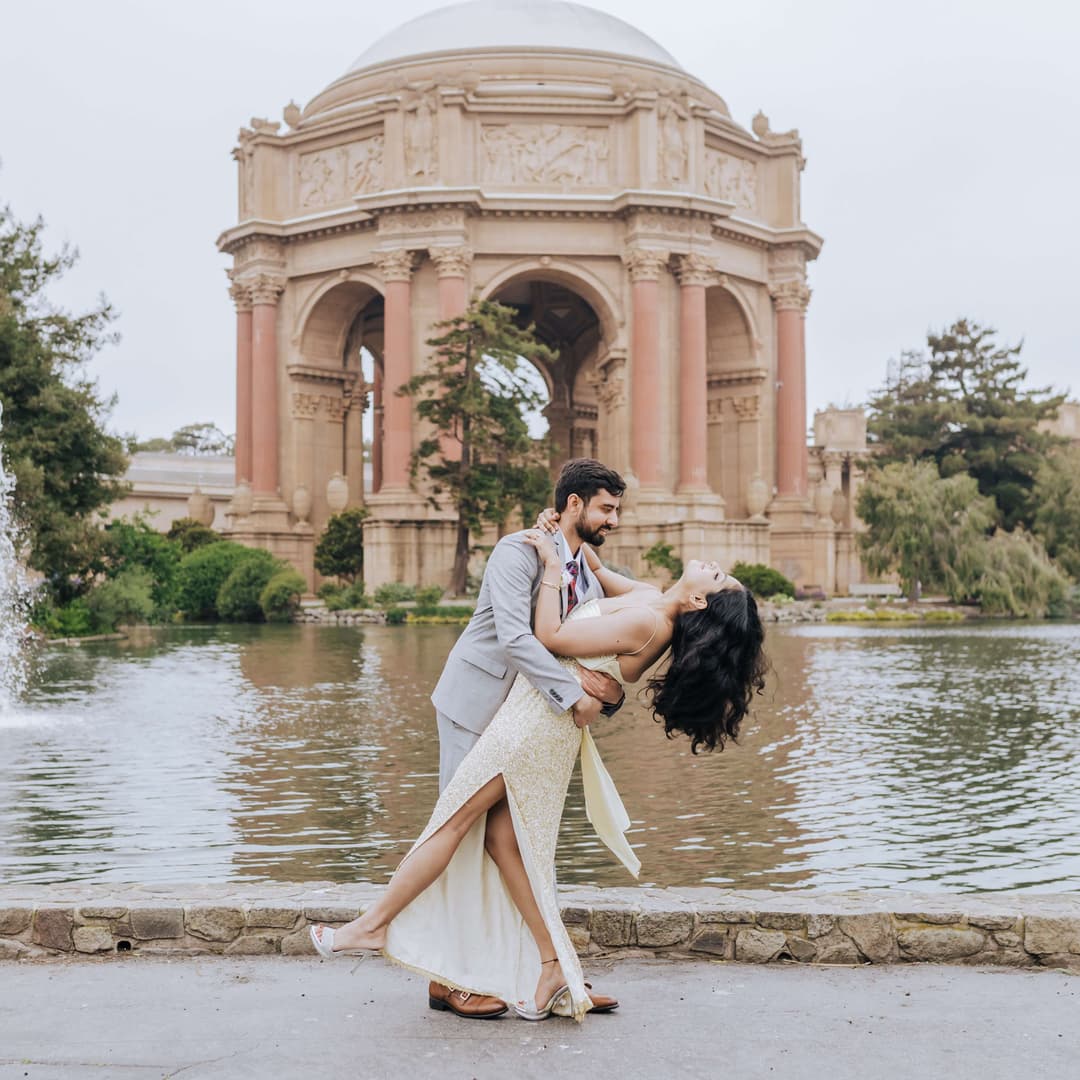 man in suit and woman in engagement dress posing in front of a famous buidling