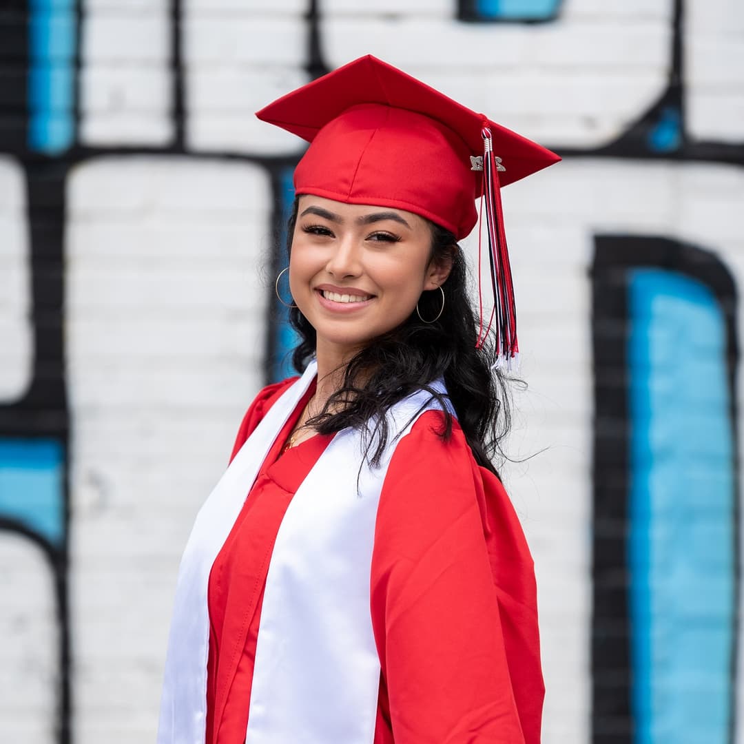 smiling woman is a graduation outfit posing in front of graffiti