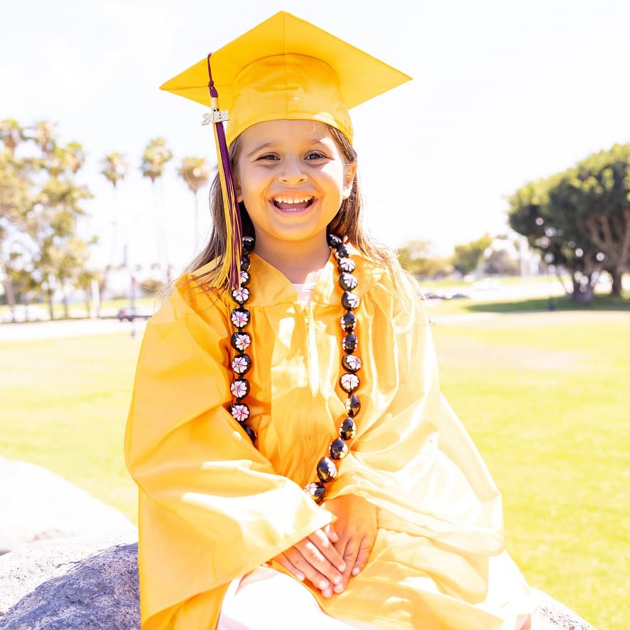 smiling girl in a grad cap and gown sitting on grass  