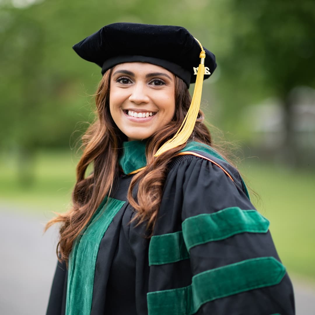 woman in a green and black grad outfit looking back and smiling