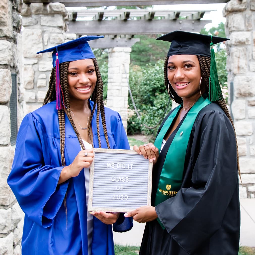 two women holding up a diploma under a stone canopy