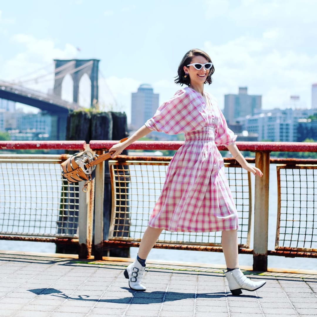 smiling woman in a checkered outfil walking next to a bridge