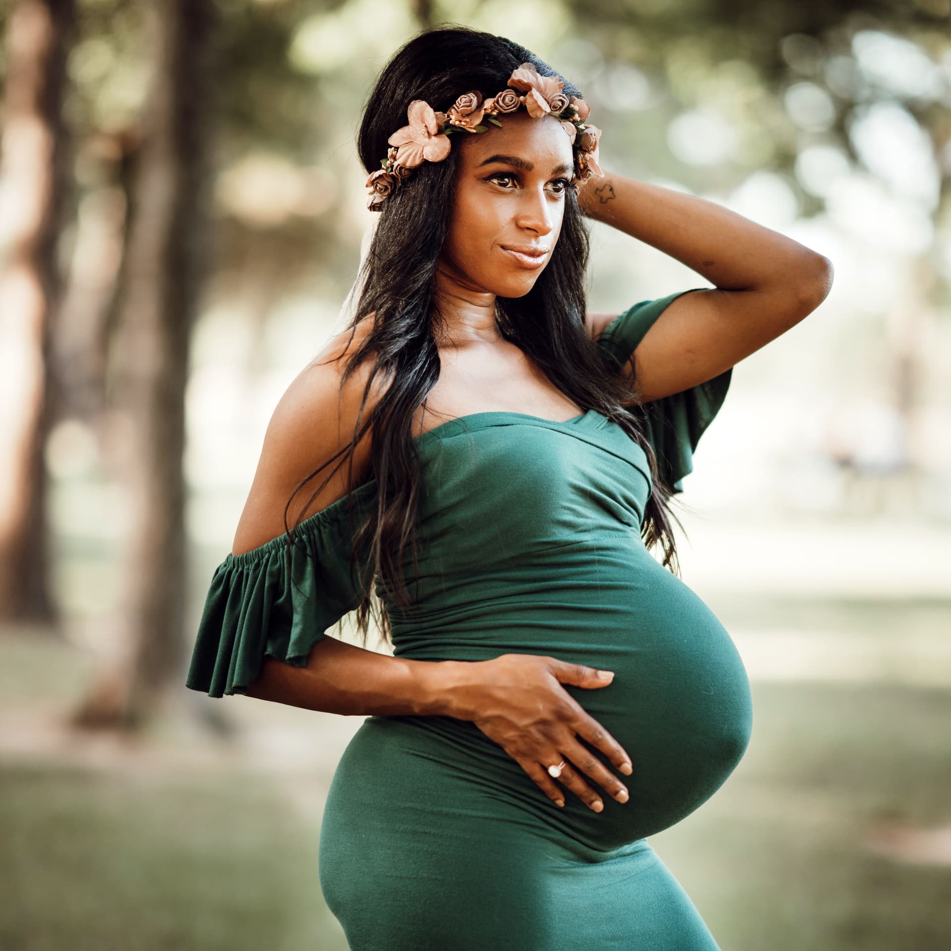 Pregnant woman in a green dress and flower crown poses for an outdoor park maternity photoshoot