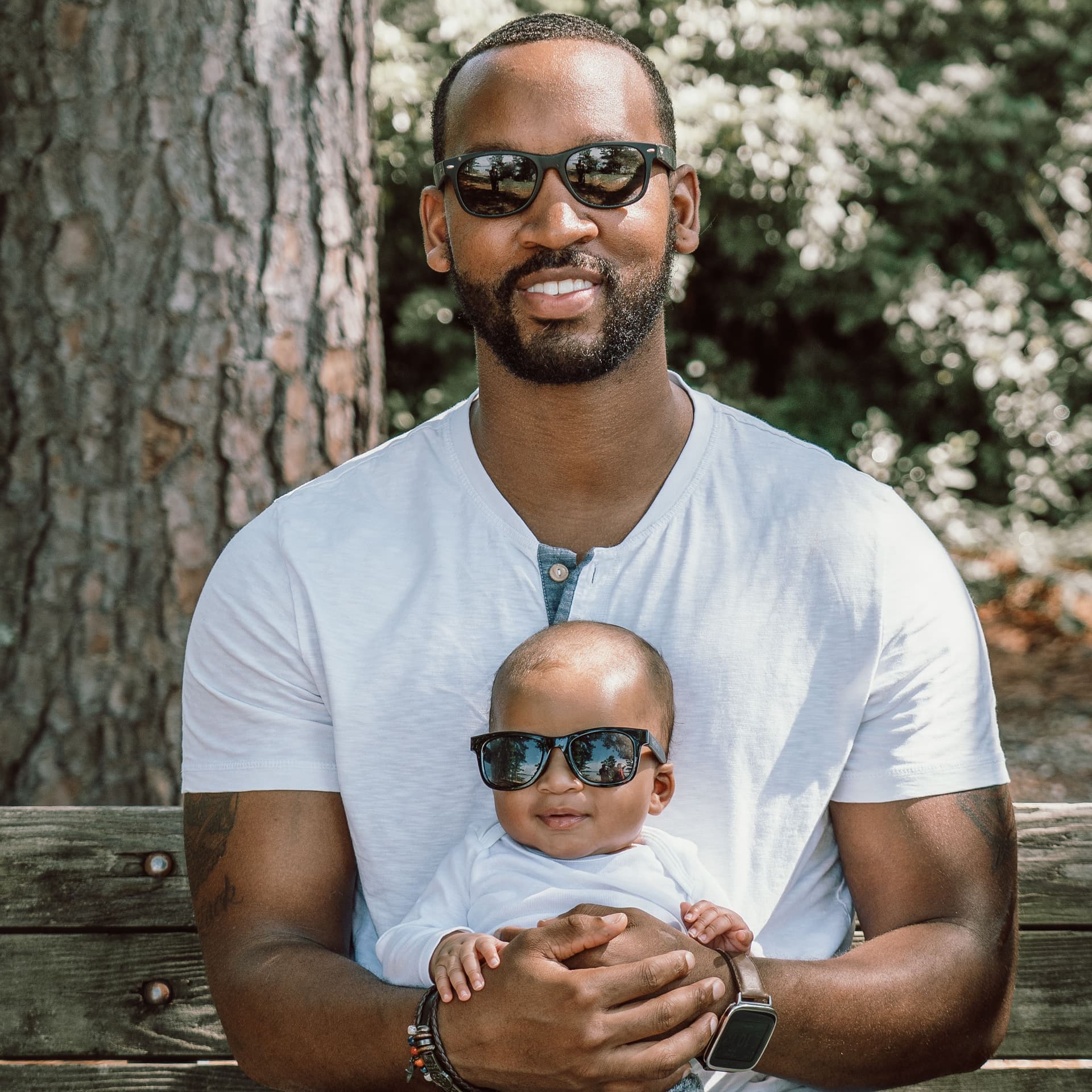 Father poses with baby in matching sunglasses on park bench for their free outdoor family photoshoot