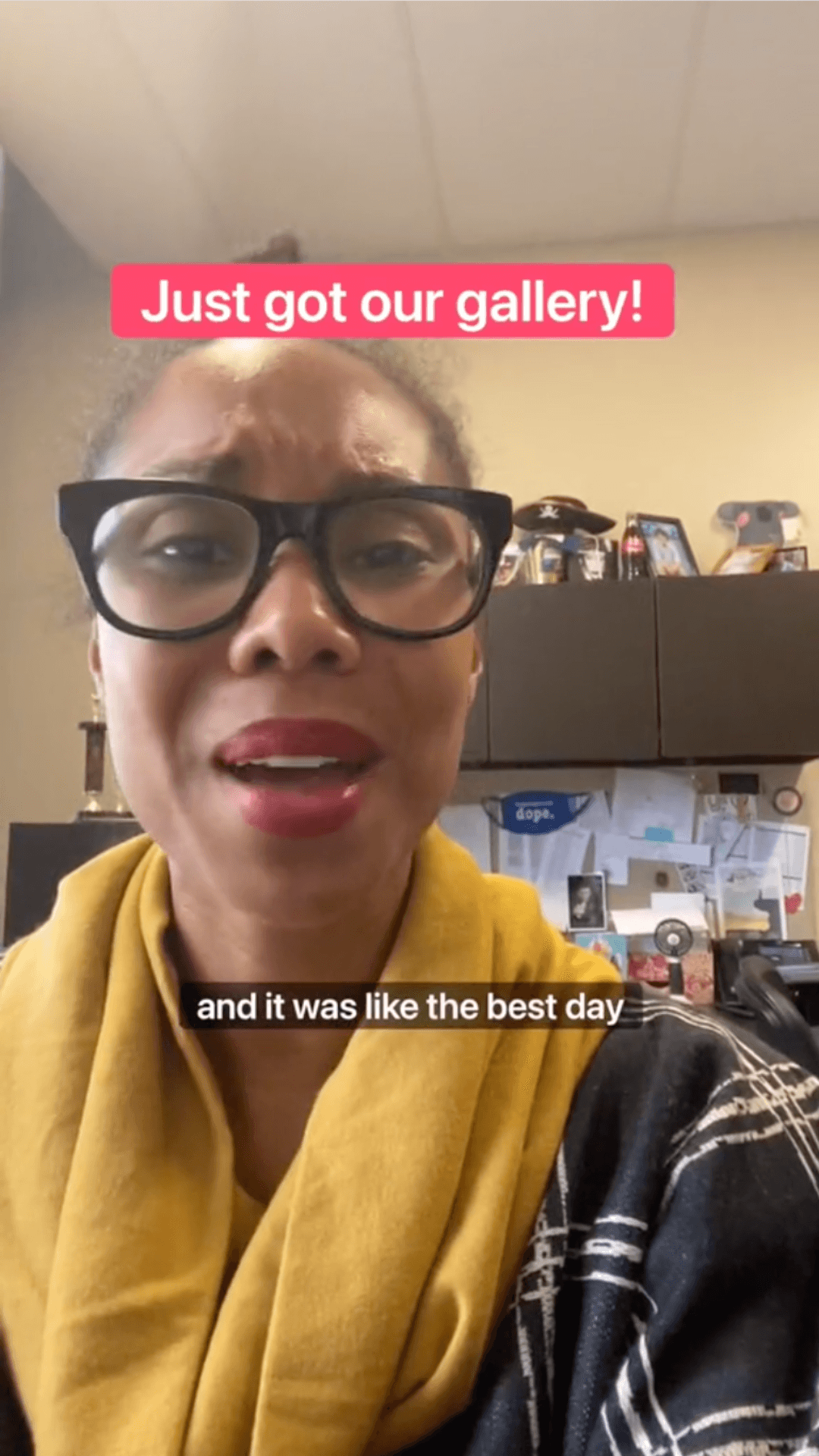 A woman with glasses and a yellow scarf speaking in an office environment with text overlays expressing joy about receiving a gallery.