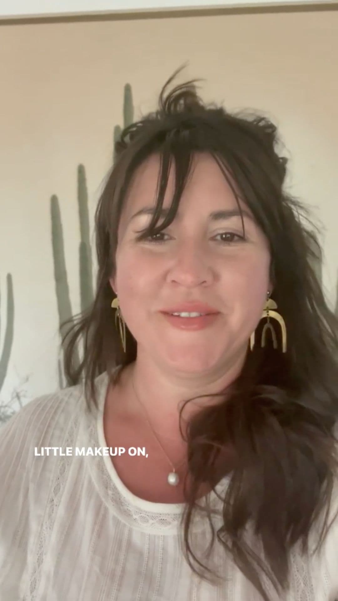 A smiling woman with dark hair wearing earrings and a white top.