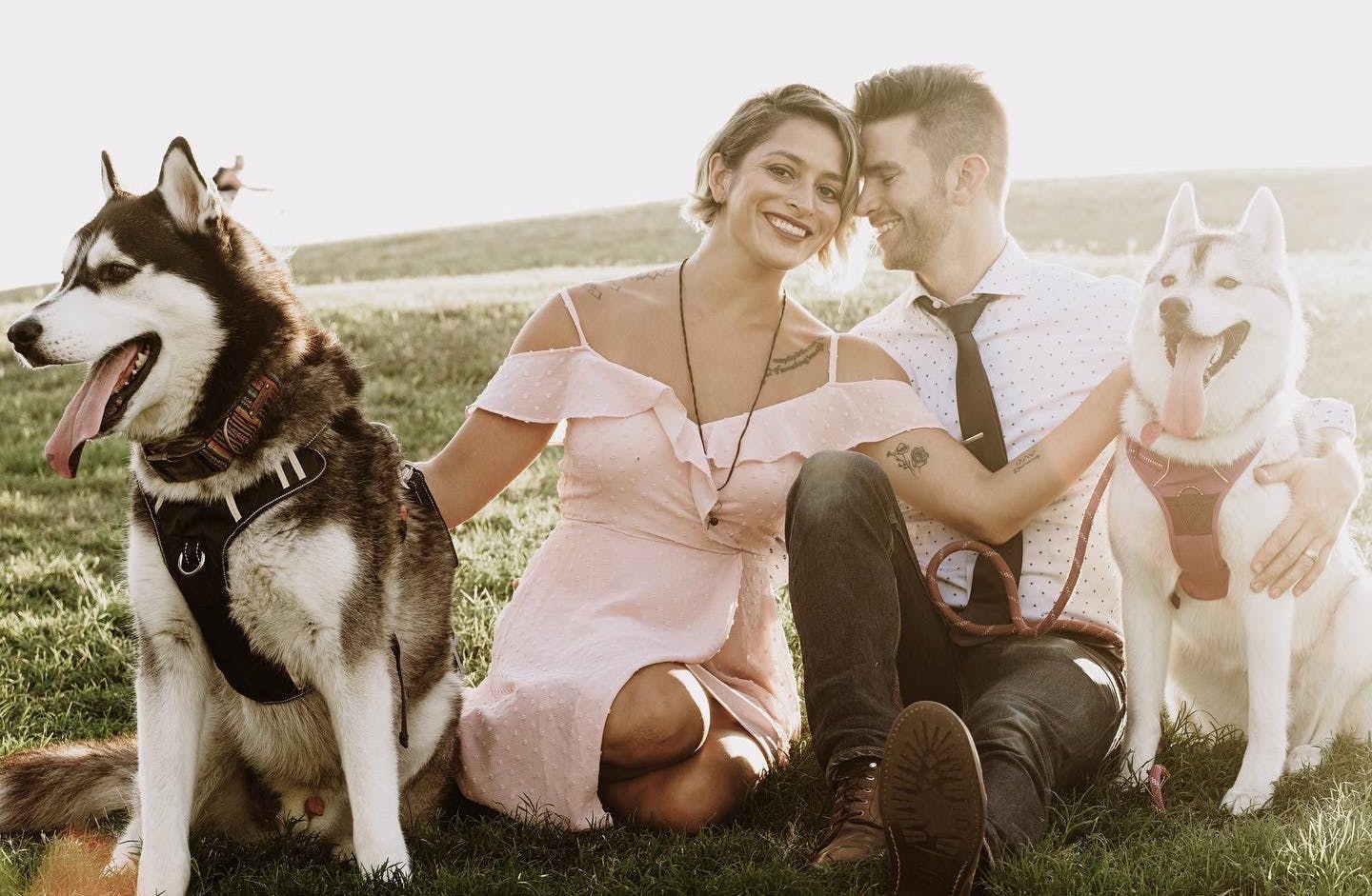 smiling couple pose with their two huskies for an outdoor pets photoshoot