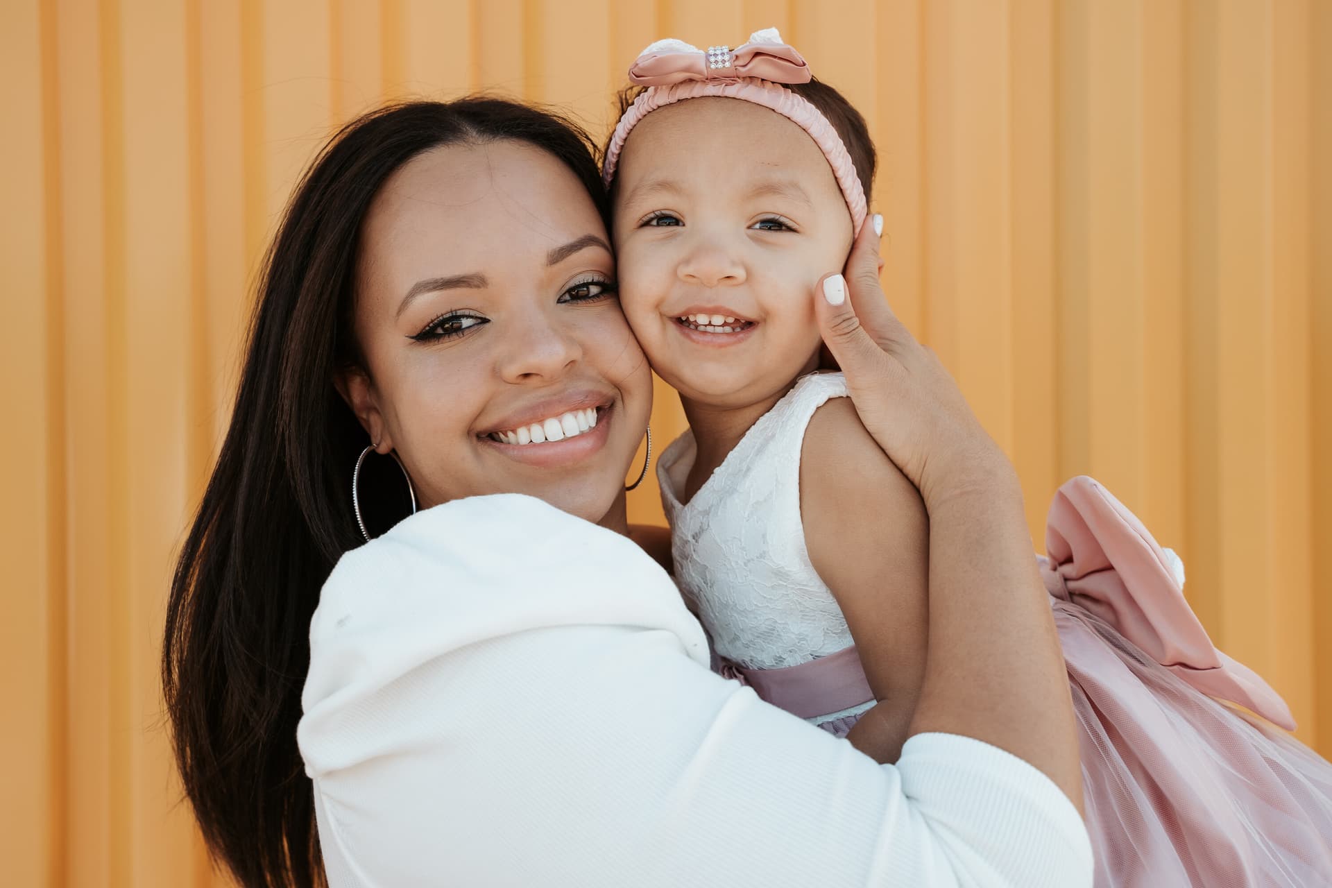 A smiling mother holding and cuddling her young toddler daughter against a warm wooden background