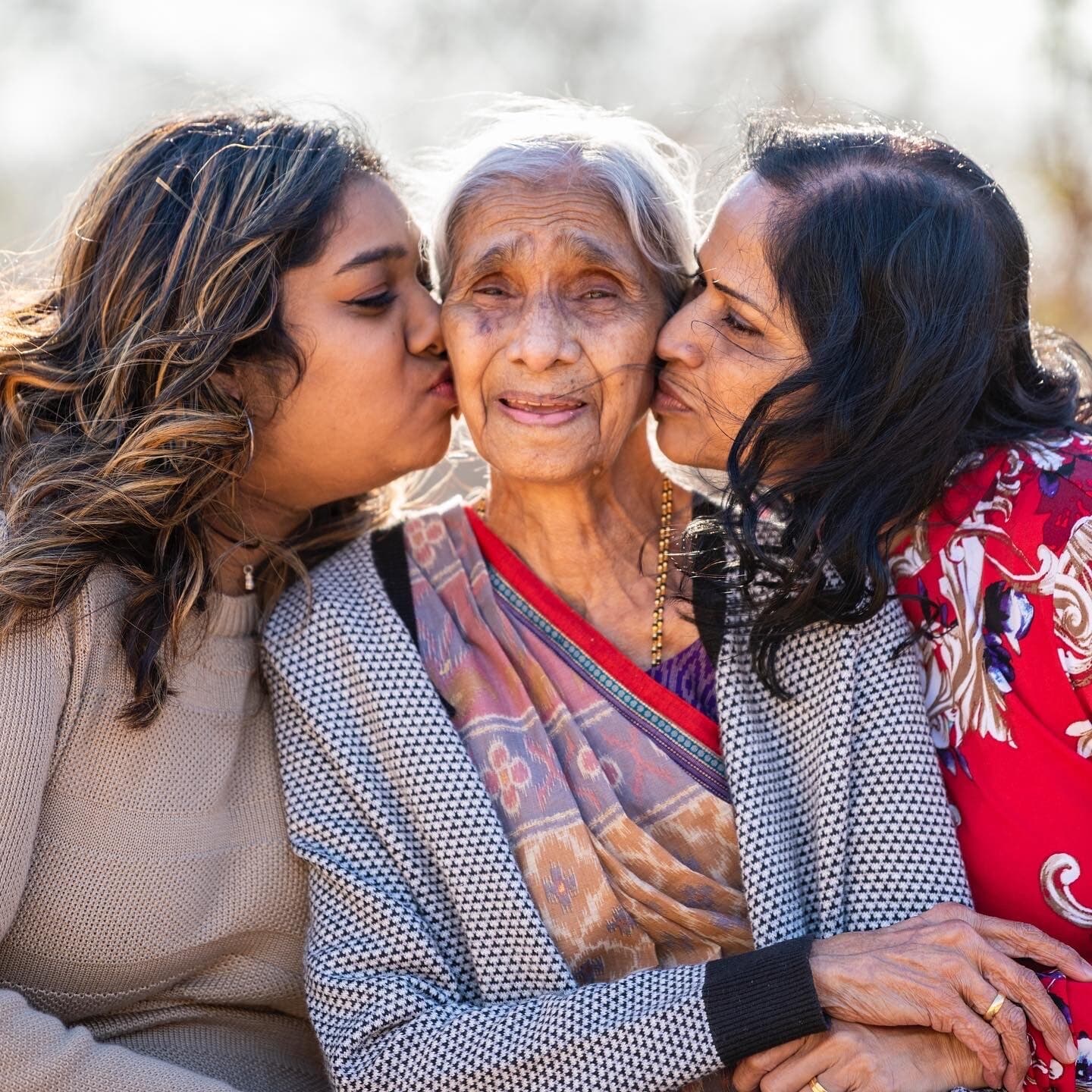 Two younger women kissing an elderly woman on each cheek, all three smiling warmly together