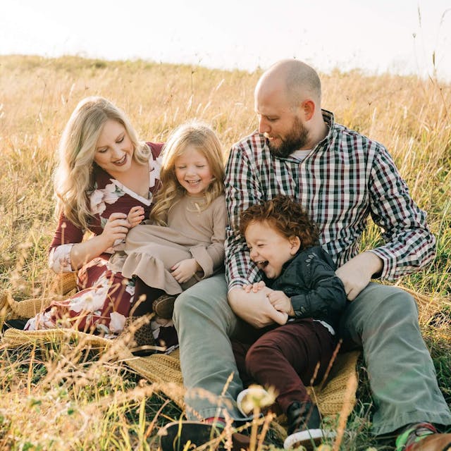 family with two kids smiling and laughing in a field for a photoshoot