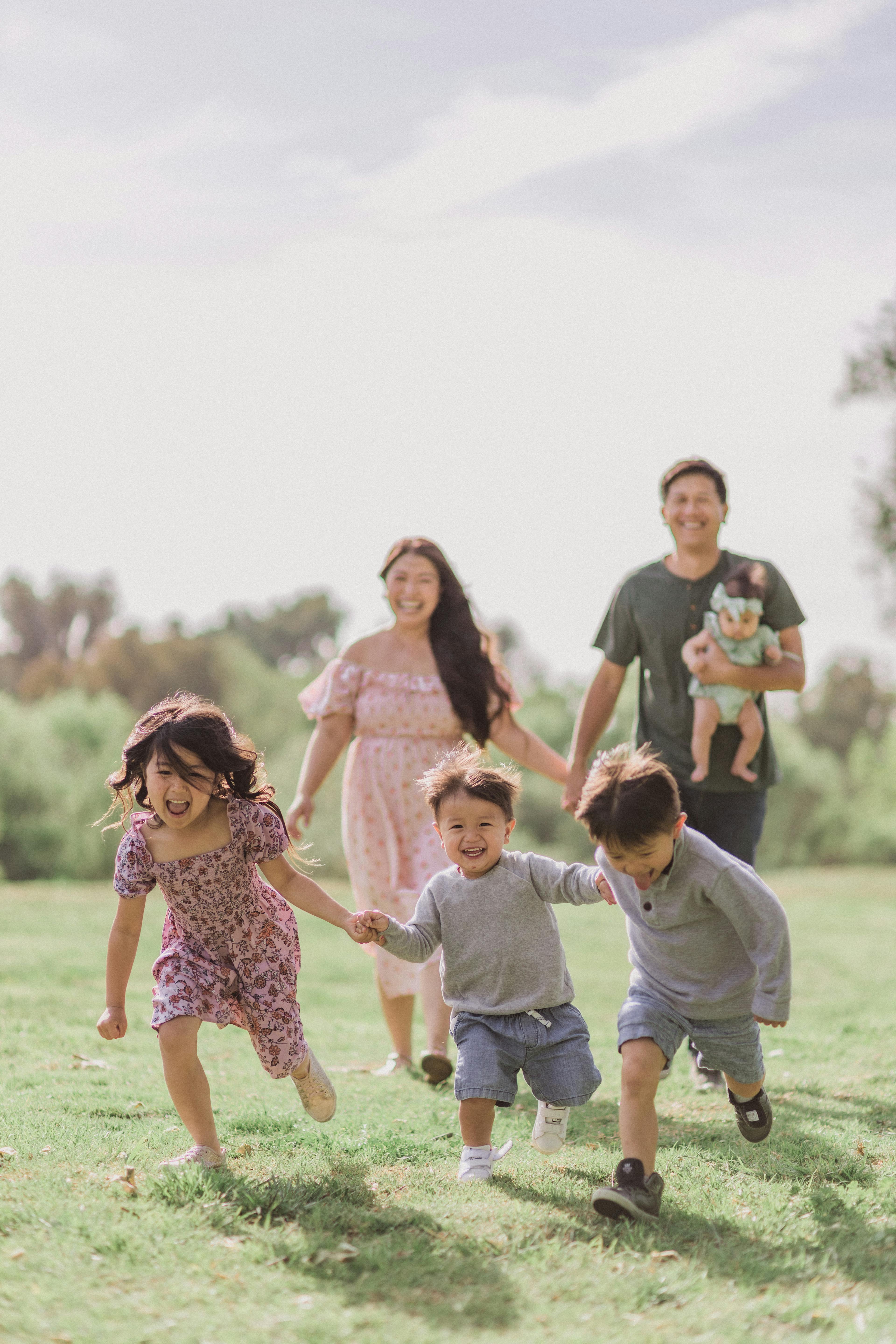 A happy family with two adults and three children running playfully on a grassy field.