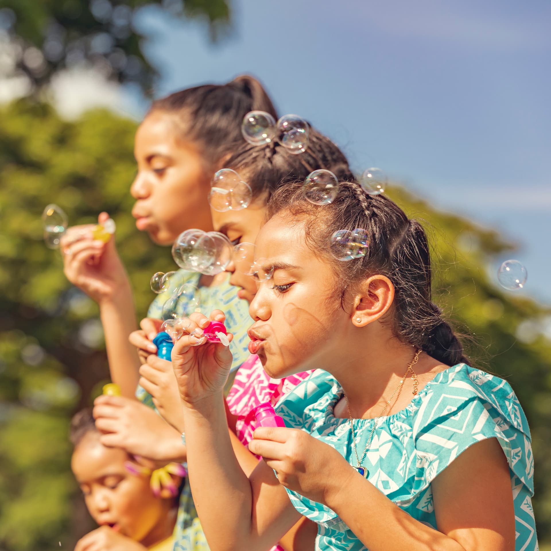Children blowing bubbles outdoors on a sunny day.