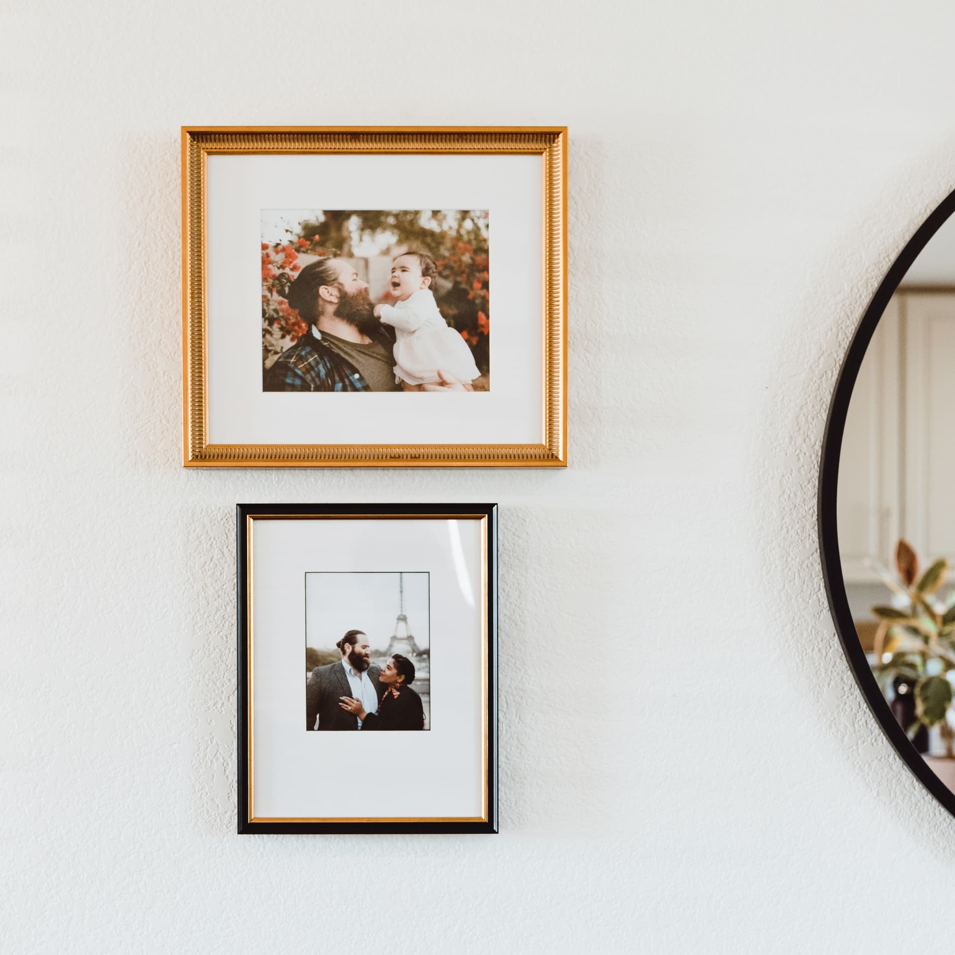Two framed photographs hanging on a wall, with a round mirror to the right.