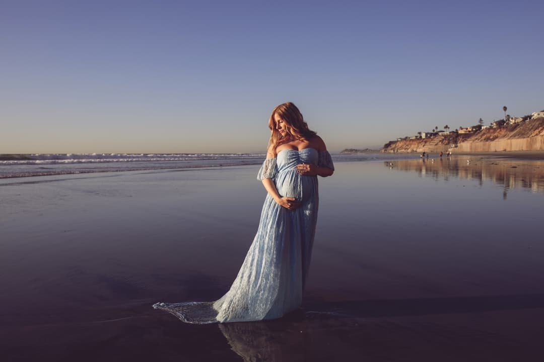 Pregnant woman standing on the beach at sunset.