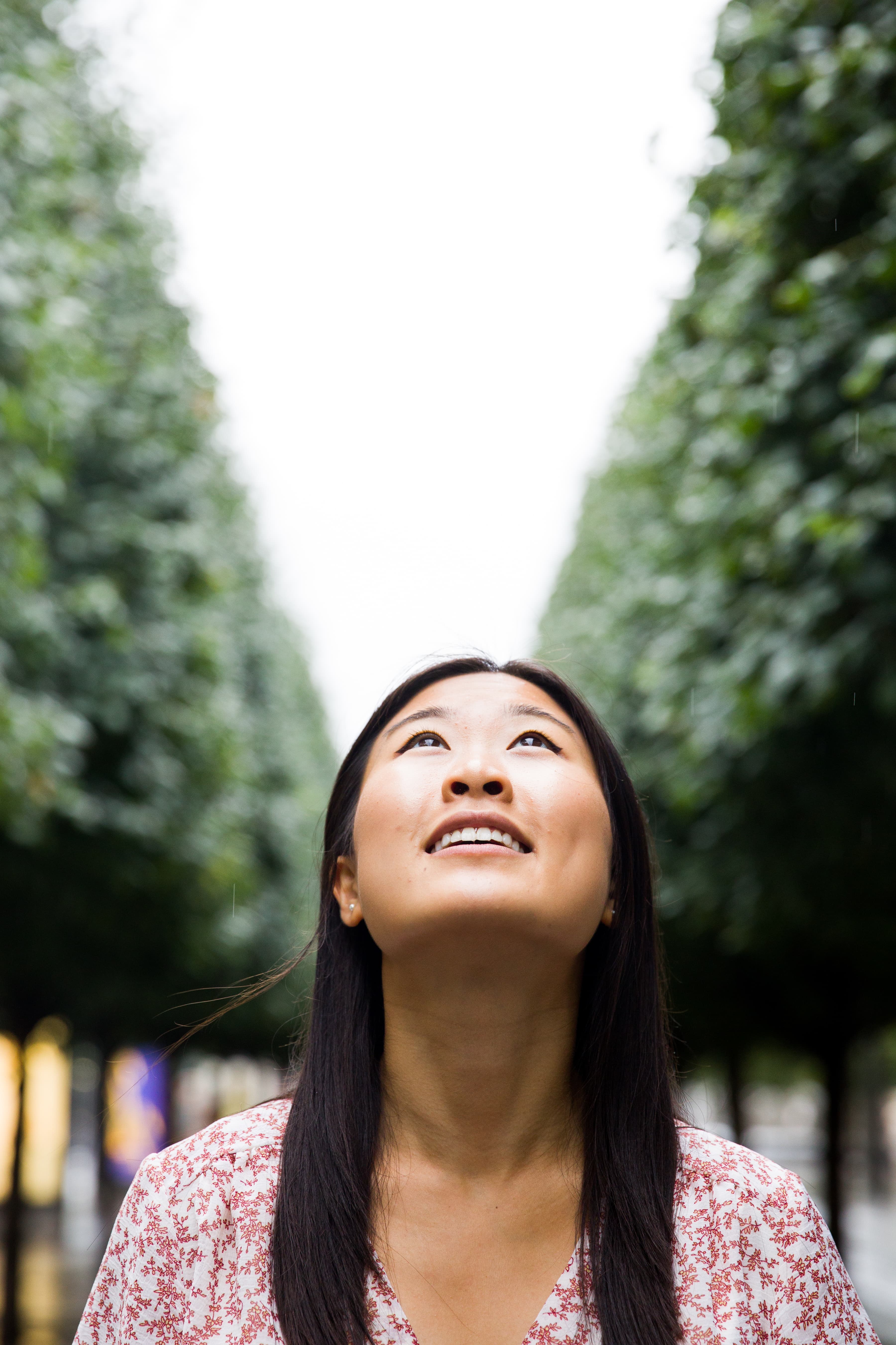 Woman looking up with a hopeful expression amidst a background of trees.