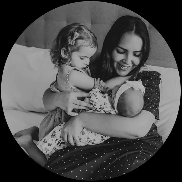 A mother embracing her two children, one a toddler and the other an infant, in a loving hug.