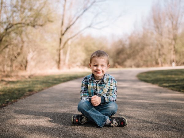 A young boy kneeling on a paved path in a park and smiling.