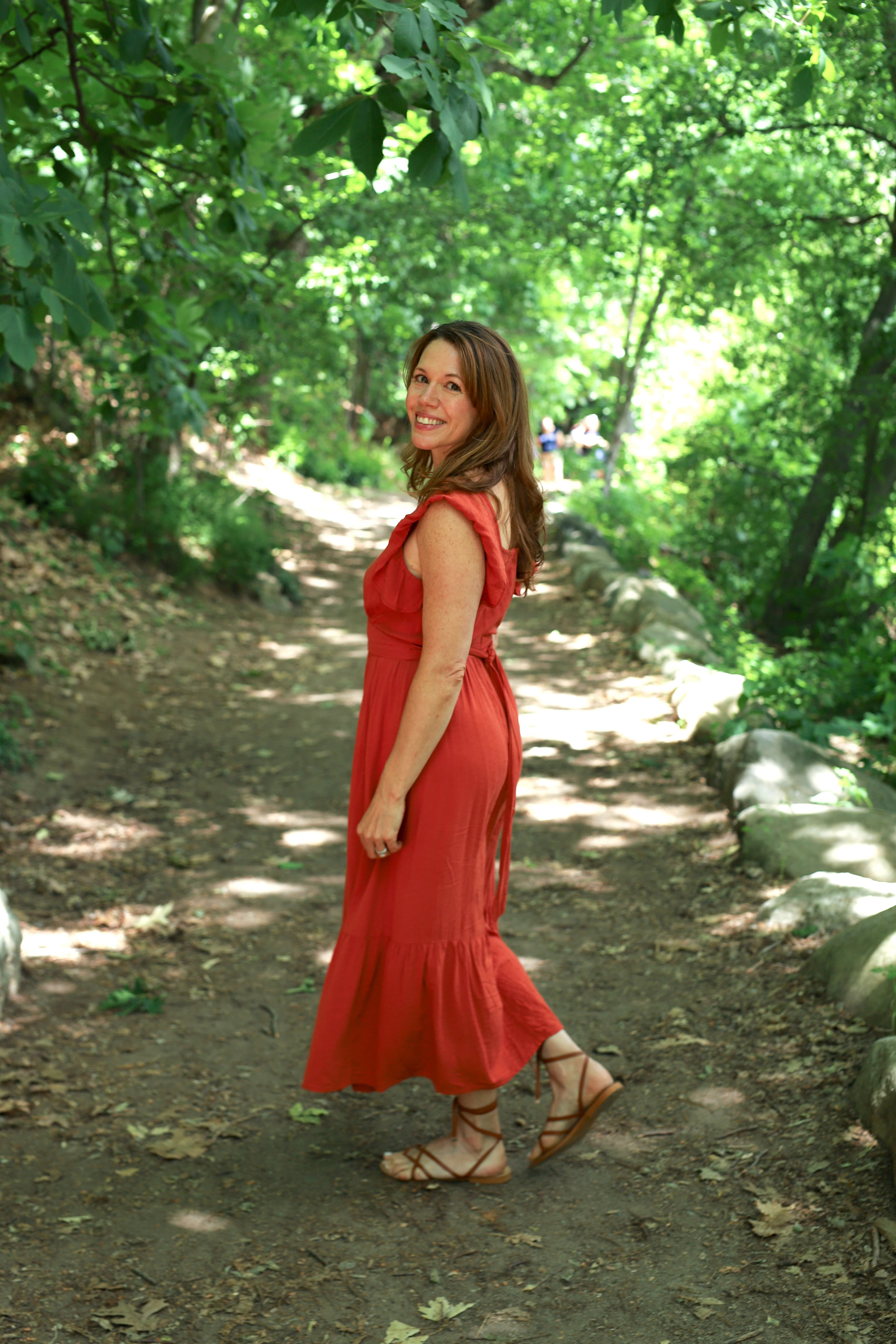 Woman in a red dress smiling over her shoulder on a forest path