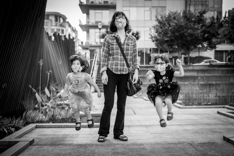 Monochrome image of a woman and two children walking and jumping on a city street