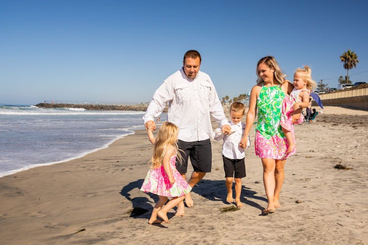 A family of five walking along the beach, with three young children and their parents.