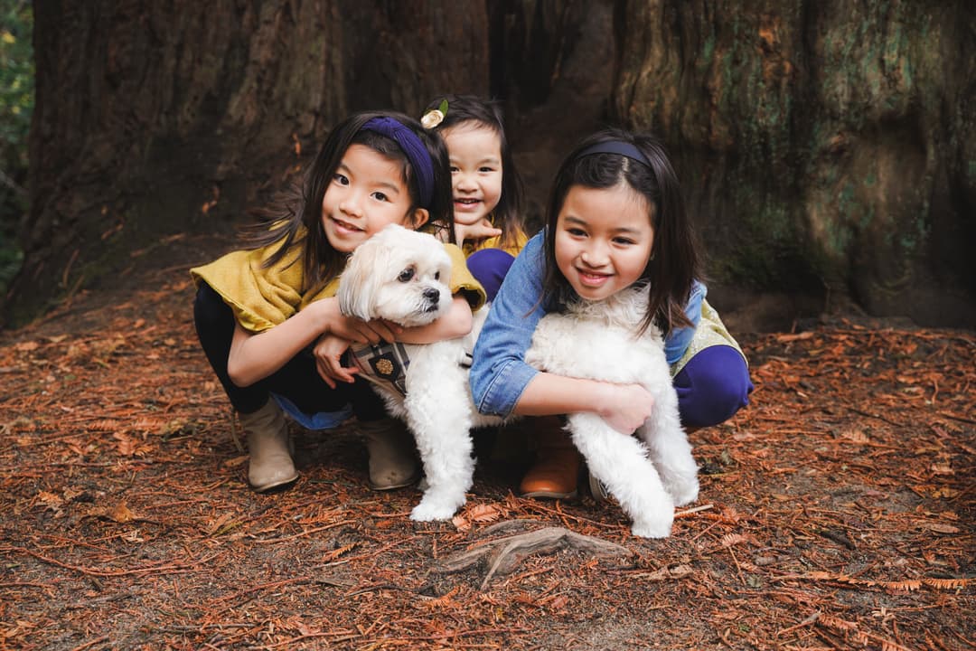 Three smiling children posing with a white dog under a large tree