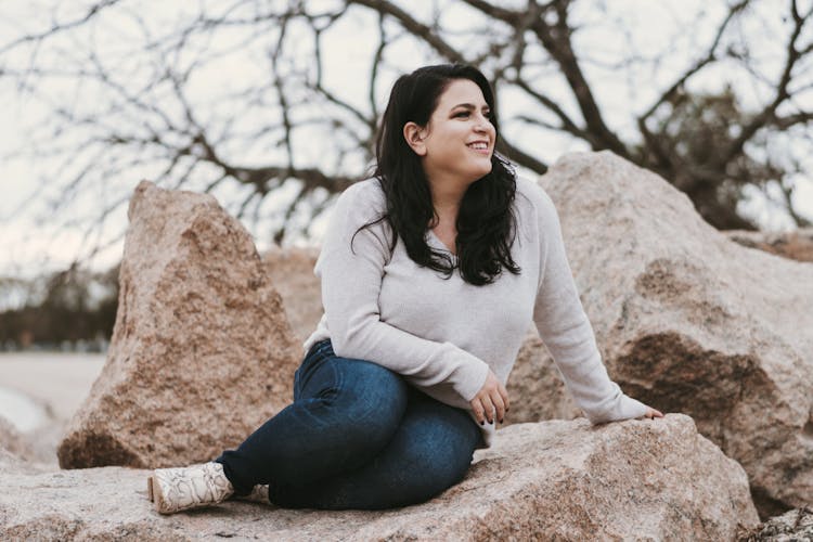 A woman smiling while sitting on large rocks outdoors.