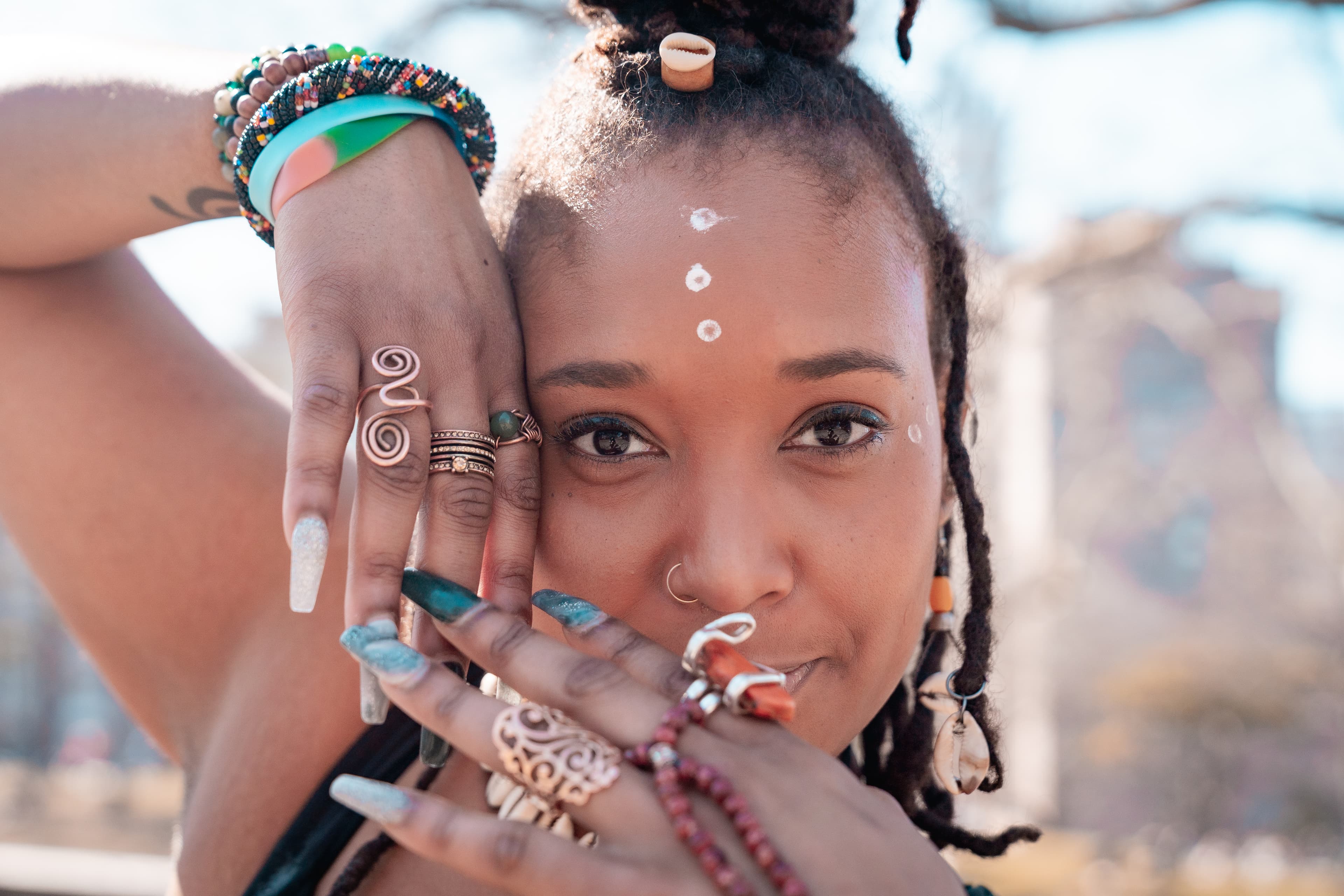 Close-up of a woman with face paint and jewelry covering half her face with her hands.