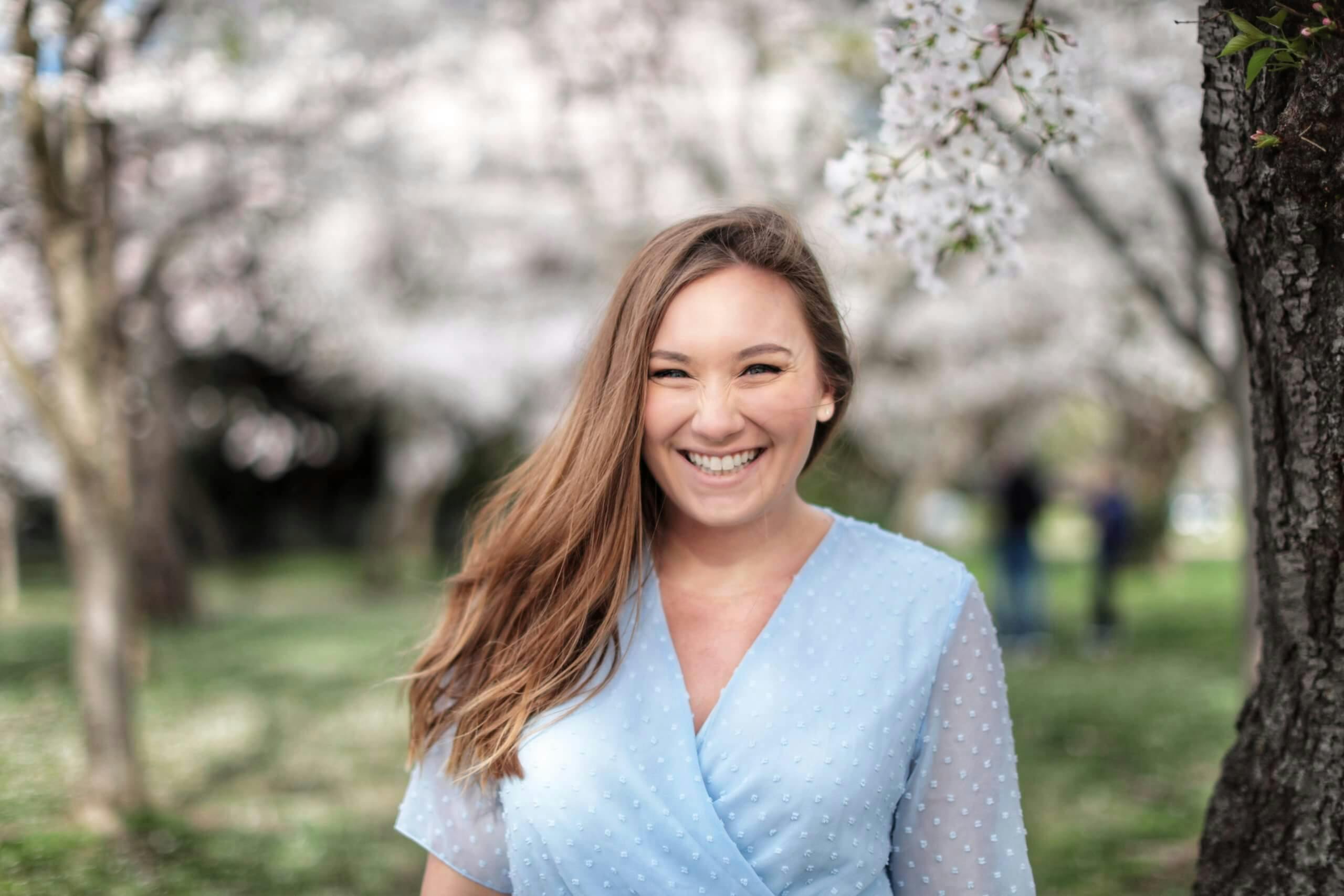 A portrait of a smiling woman with cherry blossoms in the background.