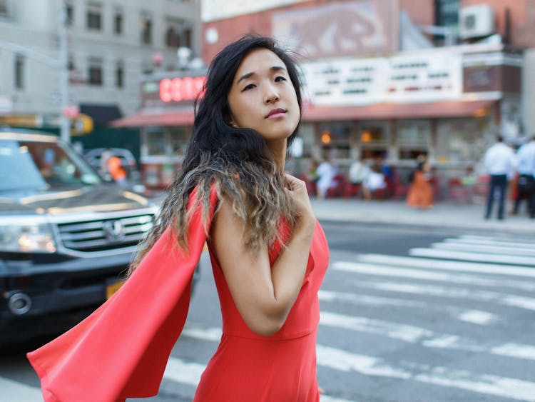 Woman in a red dress posing on a bustling city street.