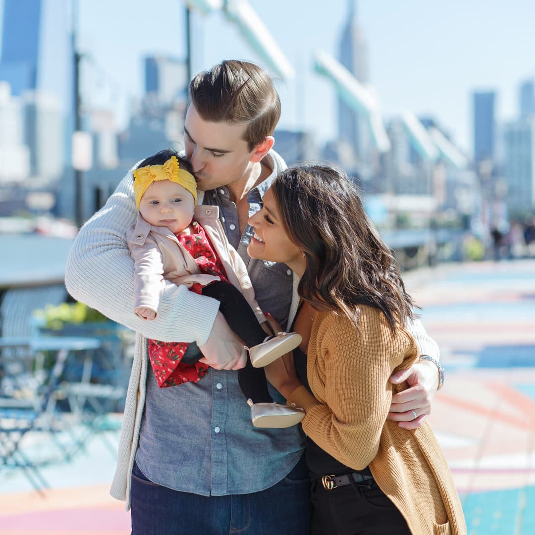 Family dotes on baby girl in front of city skyline for their free outdoor family photoshoot