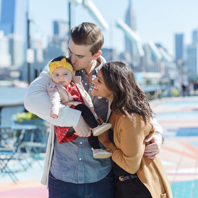 Family dotes on baby girl in front of city skyline for their free outdoor family photoshoot