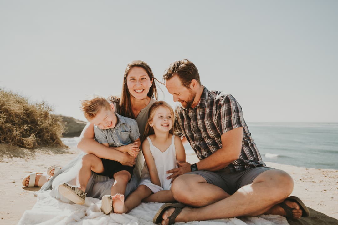 A happy family with two children sitting on a blanket at the beach.