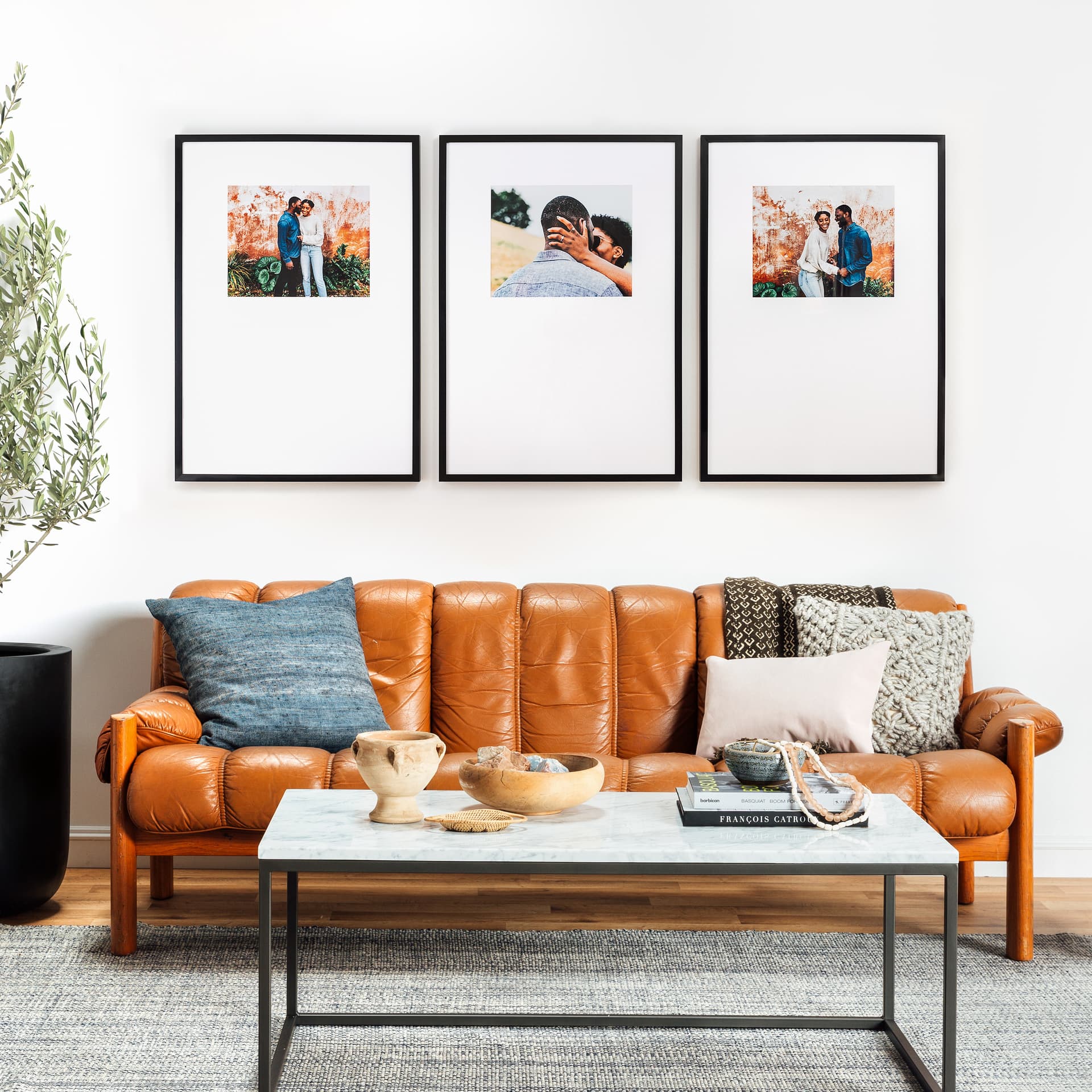 A living room with a brown leather sofa, a coffee table, and three framed pictures on the wall.