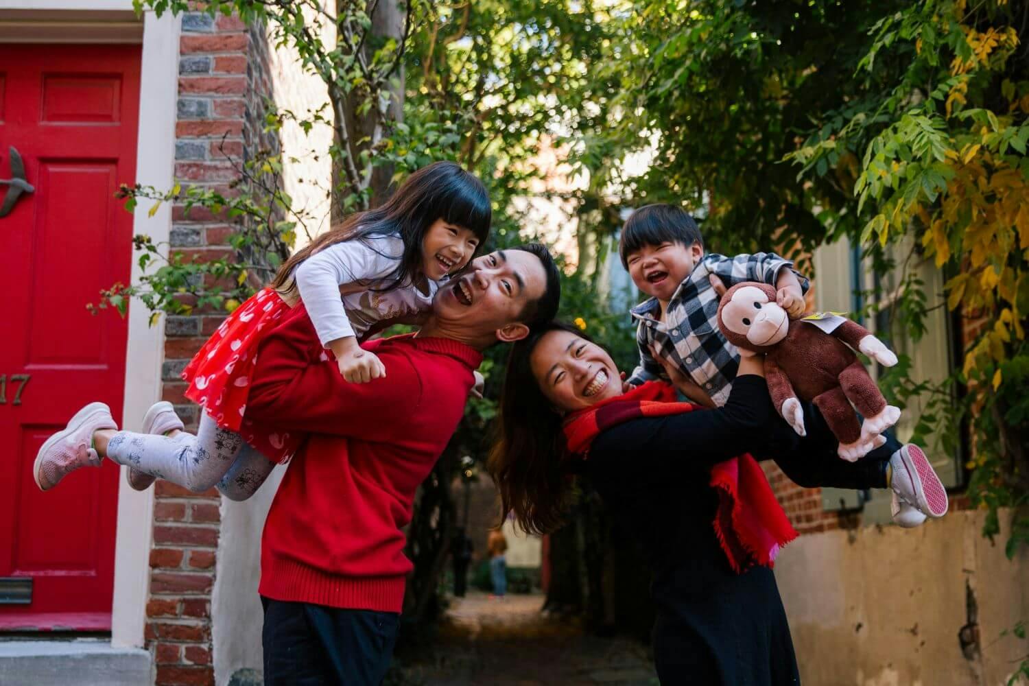 A family of four smiling and playing outside a house with red door