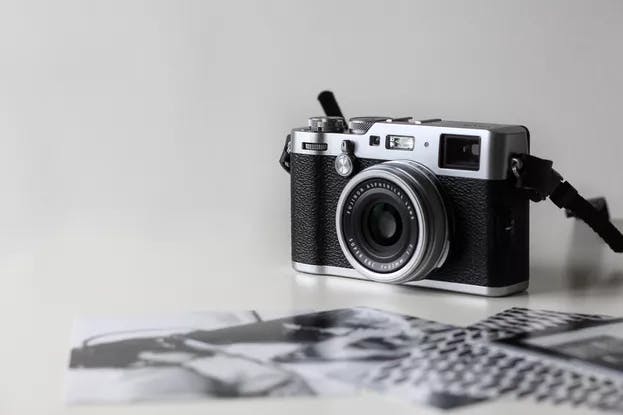A vintage camera on a table with blurred black and white photographs in the background.