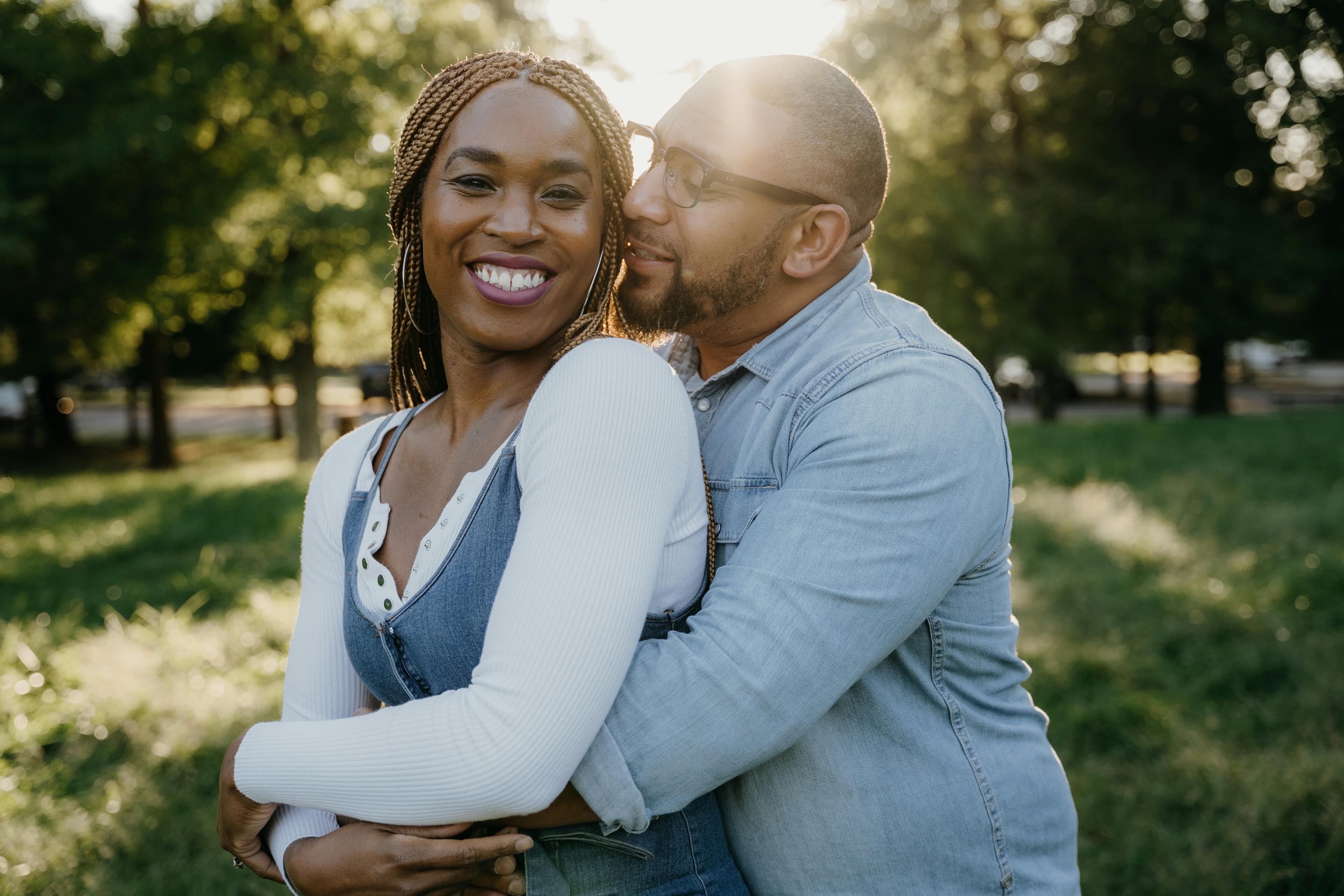 A couple embracing and smiling in the glow of sunset in a park.